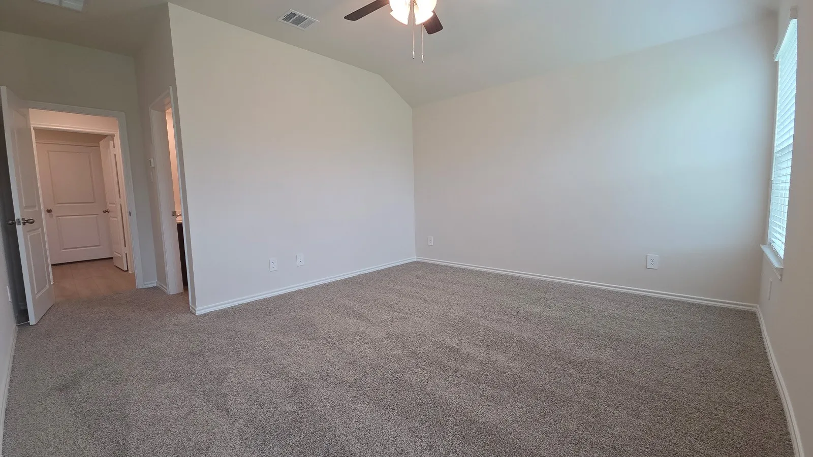 Spacious room featuring vaulted ceilings, neutral-toned carpet, and a ceiling fan