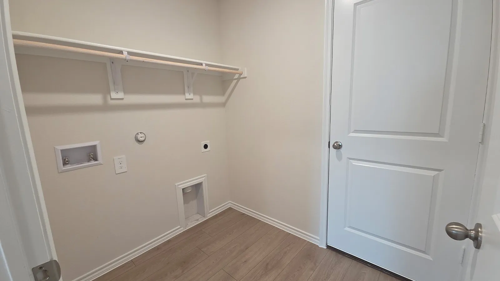 Dedicated utility space with wood-finish flooring, light neutral wall paint, and a built-in hanging rod with shelving