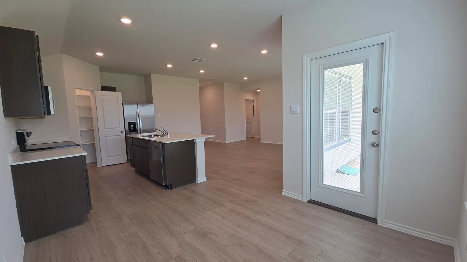 Open-concept kitchen featuring wood-finish flooring, recessed lighting, white countertops, a central island with an undermount sink, and stainless steel appliances
