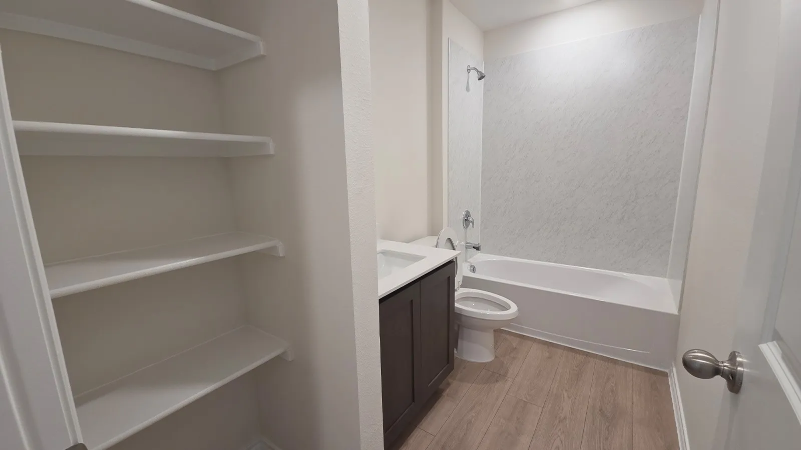 Bathroom featuring a dark wood-finish vanity with an integrated sink, a white toilet, and a white bathtub with a textured shower surround