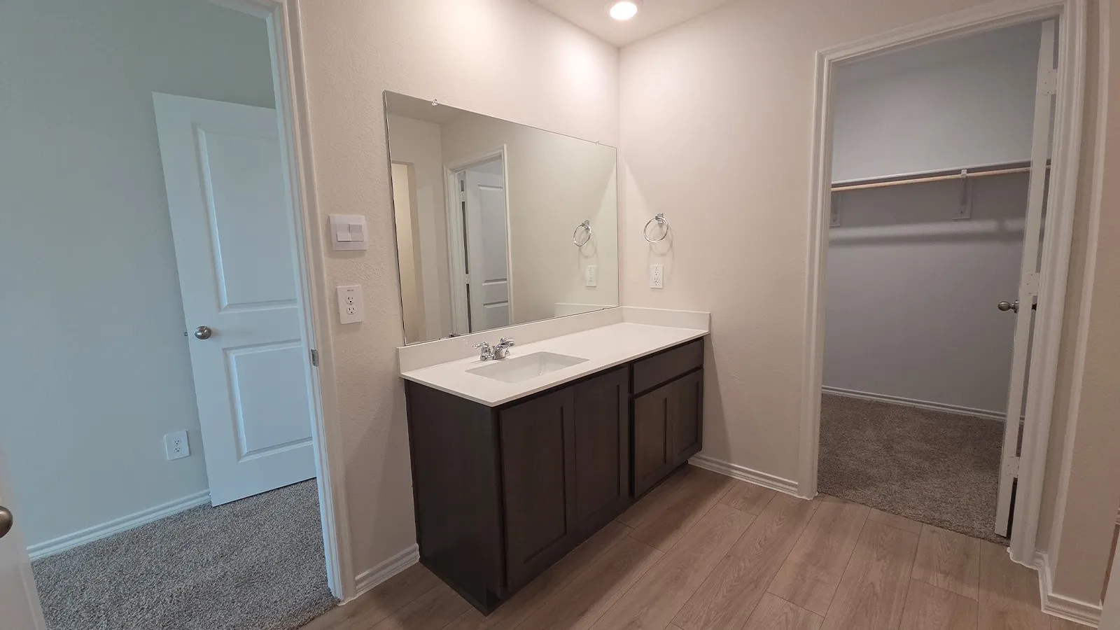 Vanity area featuring a single basin with a white countertop, dark wood-finish cabinetry, and an integrated mirror