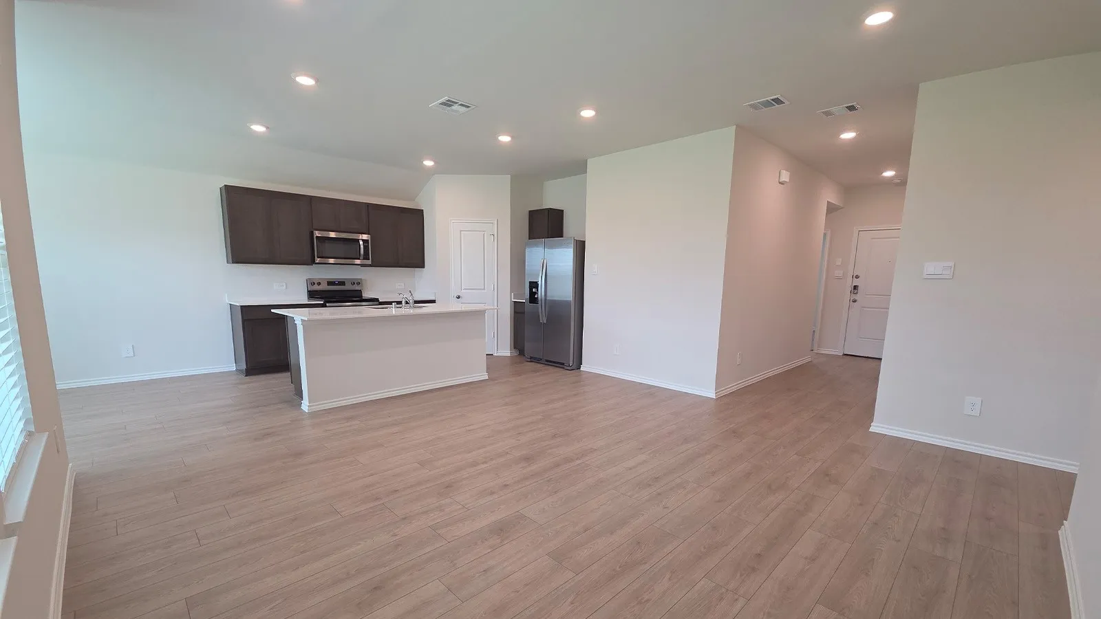 Open-concept living space with wood-finish flooring, recessed lighting, and a kitchen featuring dark wood cabinetry, white countertops, and stainless steel appliances