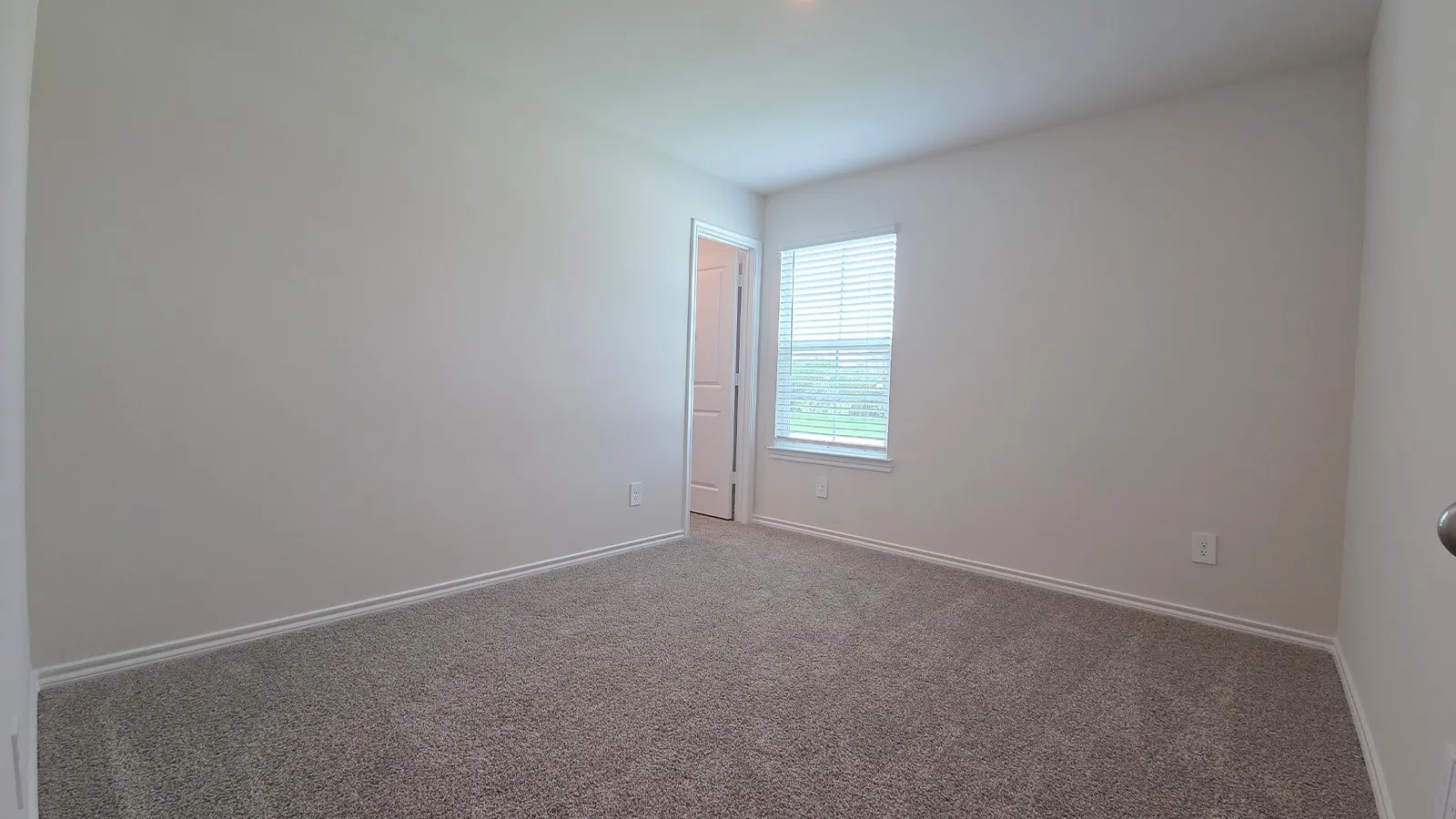 Spacious room featuring neutral carpeting, light-toned walls, and a window with horizontal blinds