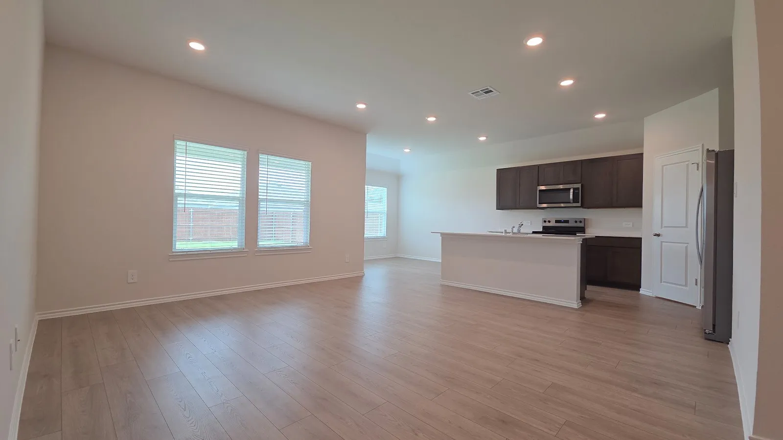 Open-concept living area featuring wood-finish flooring, recessed lighting, and multiple windows with blinds