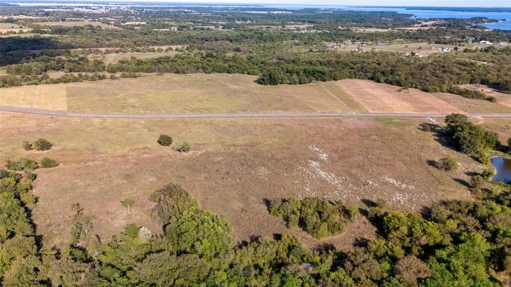 Expansive land parcel featuring open fields, scattered mature trees, and a visible road frontage