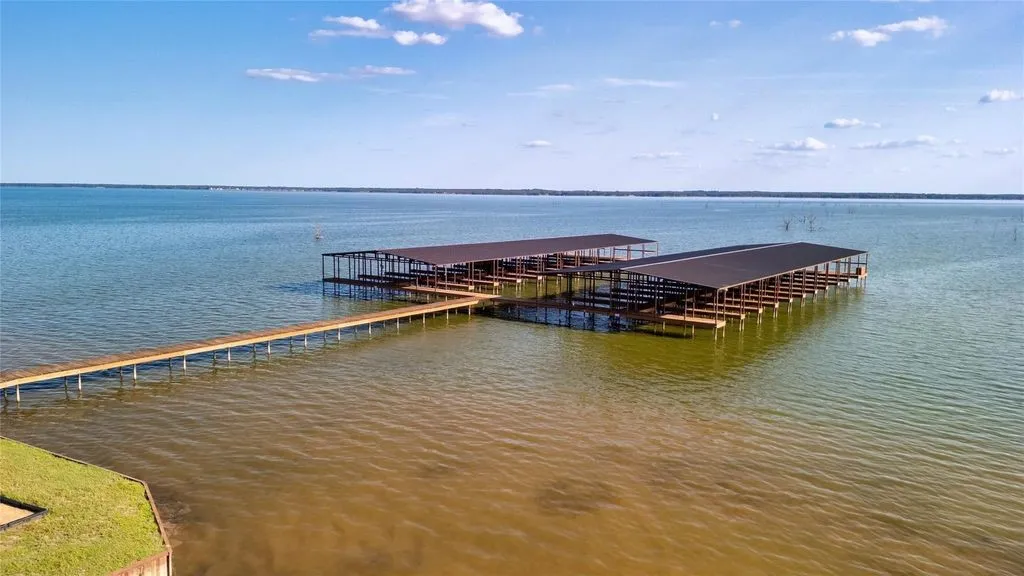 Expansive lakefront with a private wooden pier extending to two covered multi-slip boat docks