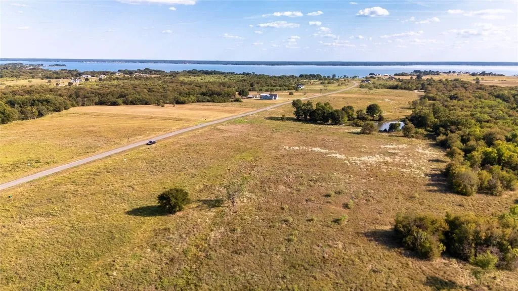 Expansive parcel featuring a paved road, natural grasslands, mature trees, and a distant body of water