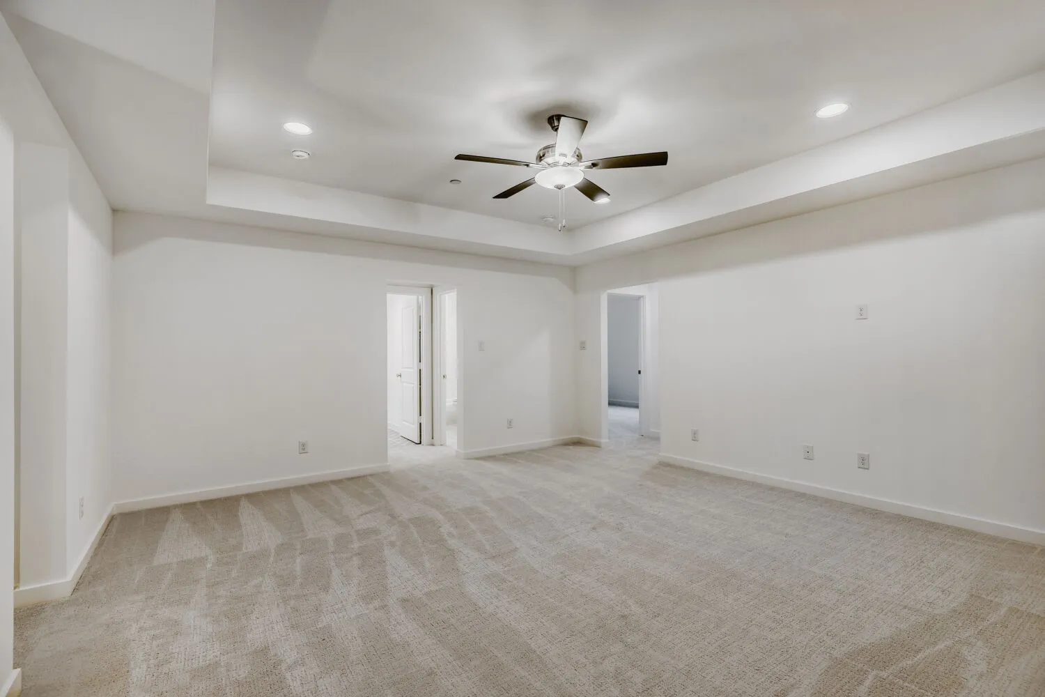Spacious room featuring neutral carpeting, white walls, a tray ceiling with a ceiling fan, recessed lighting, and white baseboards