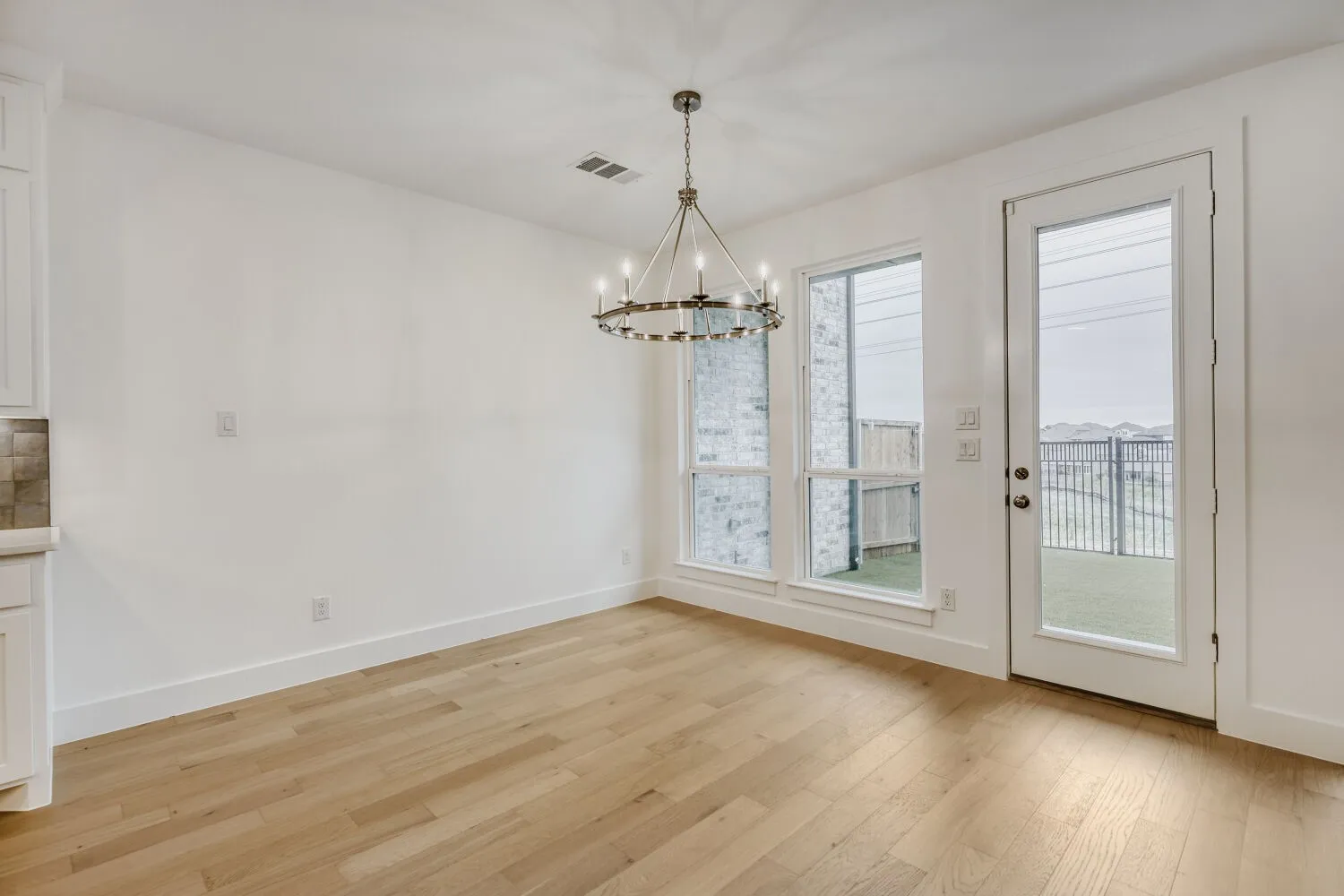Spacious room featuring wood-finish flooring, a contemporary chandelier, and white baseboards