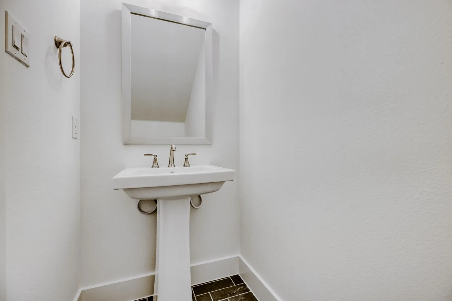 Pedestal sink with brushed nickel faucet, framed mirror, and dark tile flooring