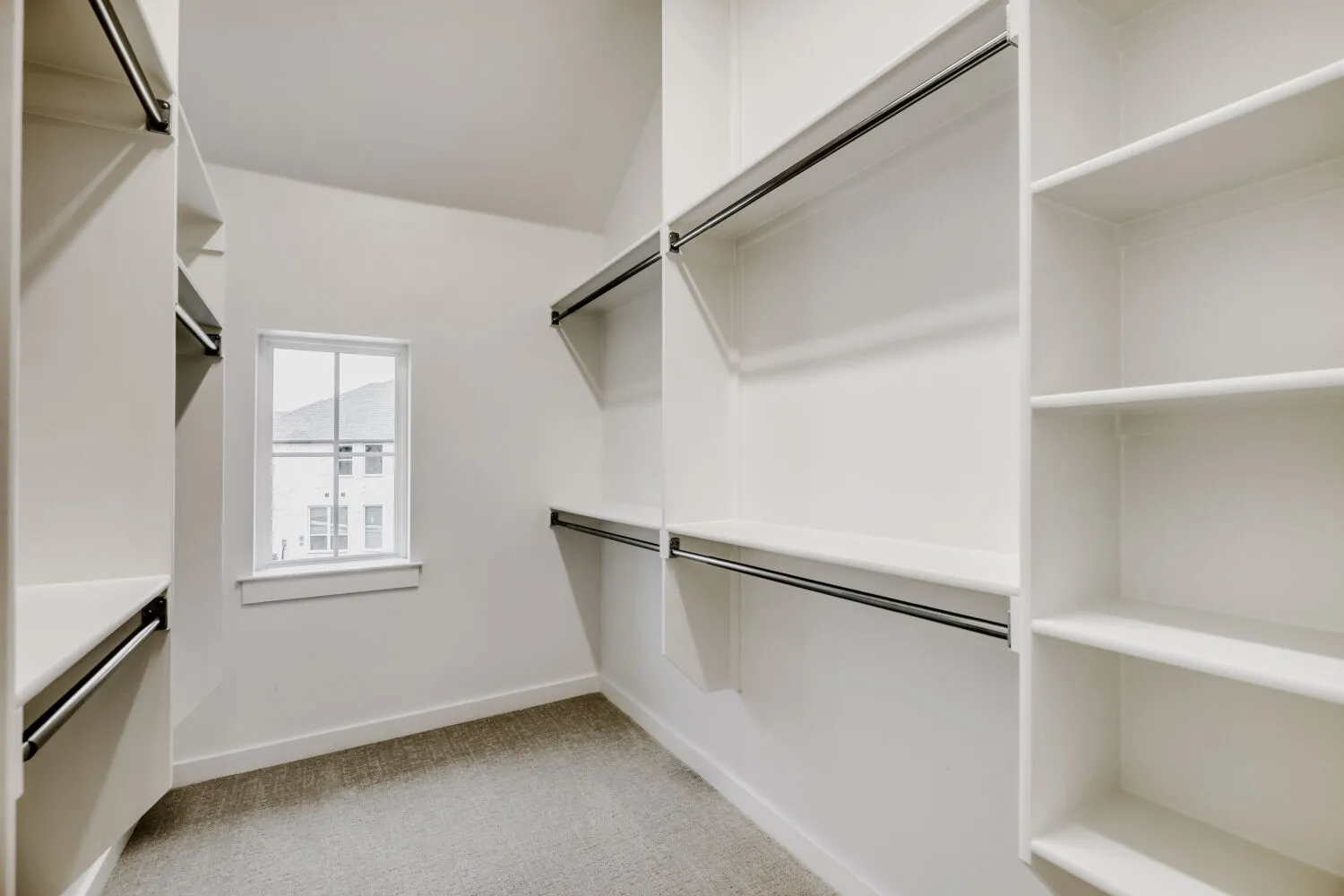 Walk-in closet featuring white built-in shelving, multiple hanging rods, and a window for natural illumination