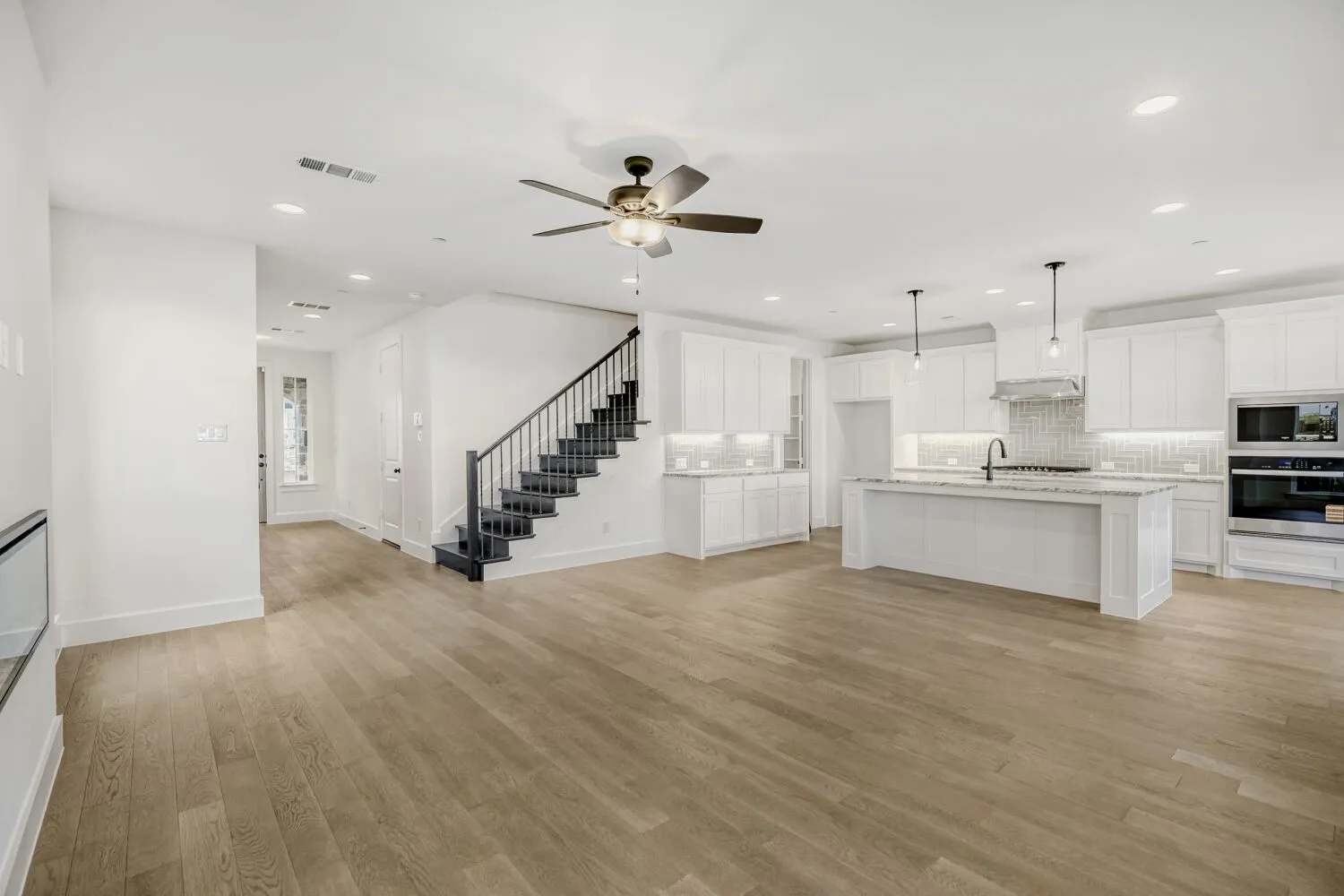Open-concept living space featuring wood-finish flooring, a contemporary kitchen, a staircase with dark banisters, recessed lighting, and a ceiling fan