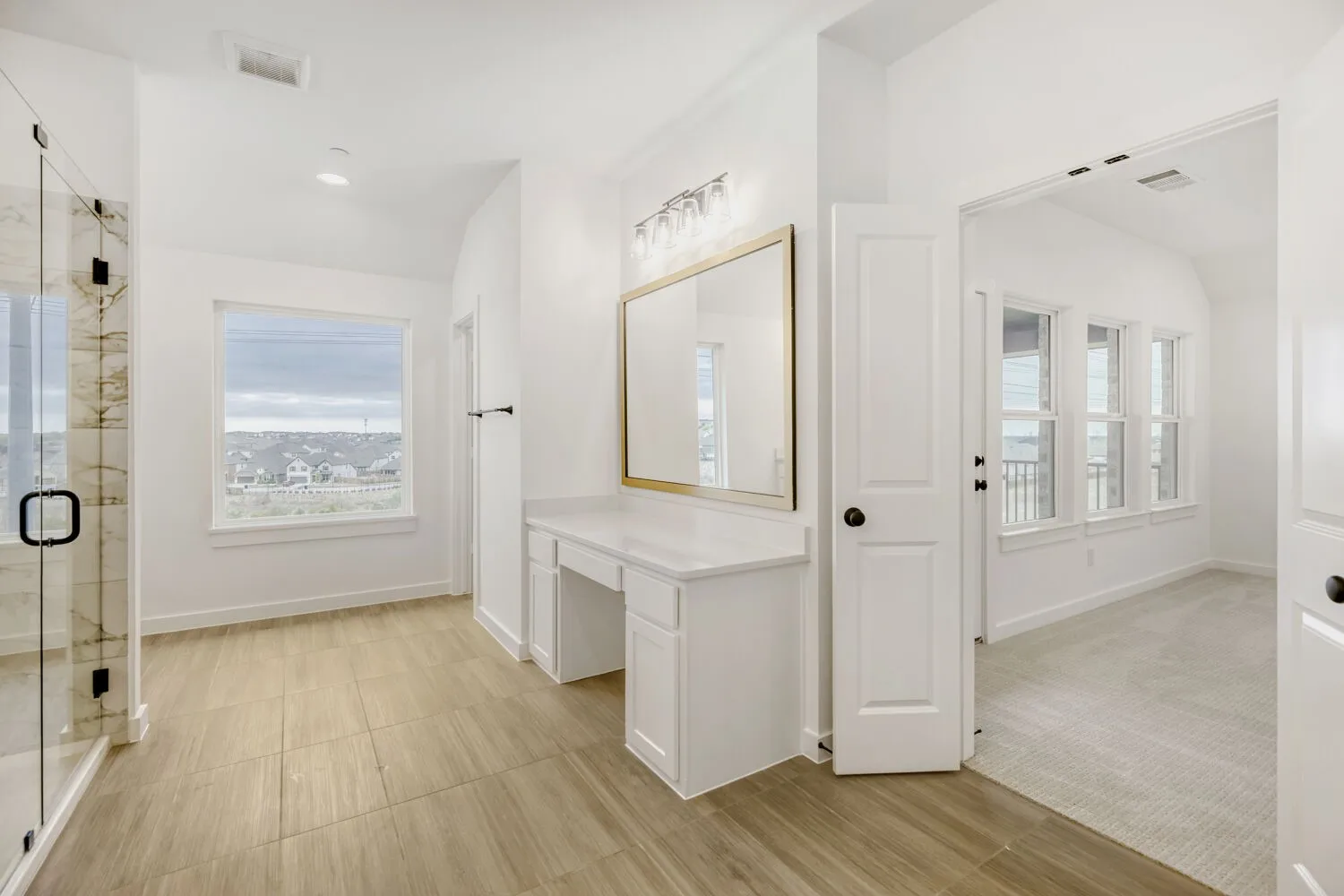 Spacious bathroom featuring a glass-enclosed shower with stone-look tile, wood-finish flooring, a vanity with a white countertop and built-in drawers, and a large window