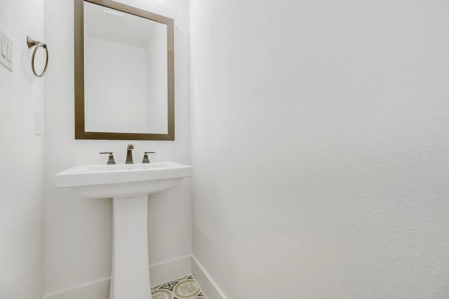 Pedestal sink with dark-toned fixtures and a coordinating framed mirror
