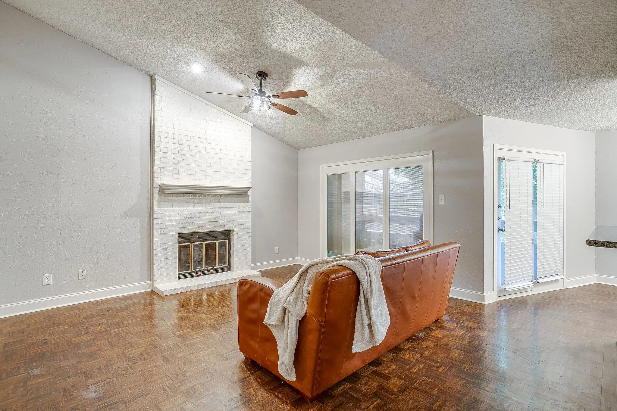 Living area featuring a white-painted brick fireplace with mantel, wood-finish parquet flooring, and a vaulted ceiling with a ceiling fan
