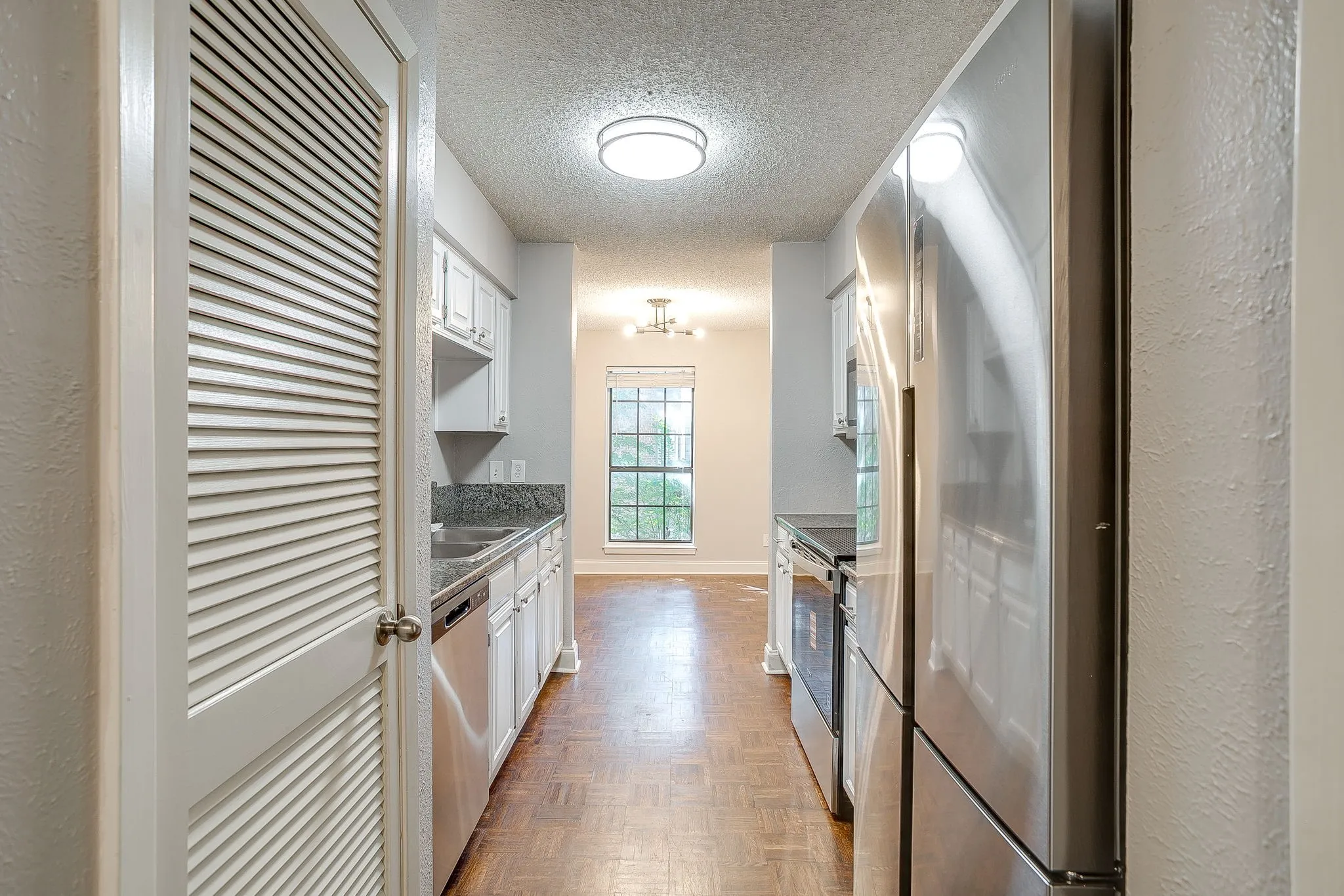 Galley kitchen featuring white cabinetry, stainless steel appliances, and dark speckled countertops