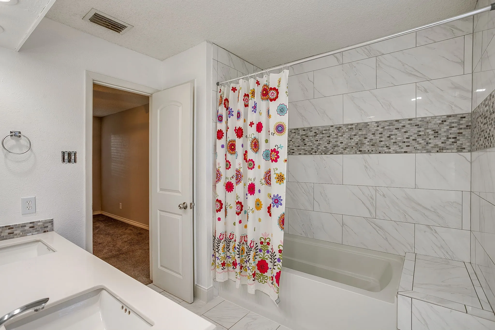 Bathroom featuring a tub/shower combination with large format white tile surround, mosaic accent tiling, and an integrated shower bench