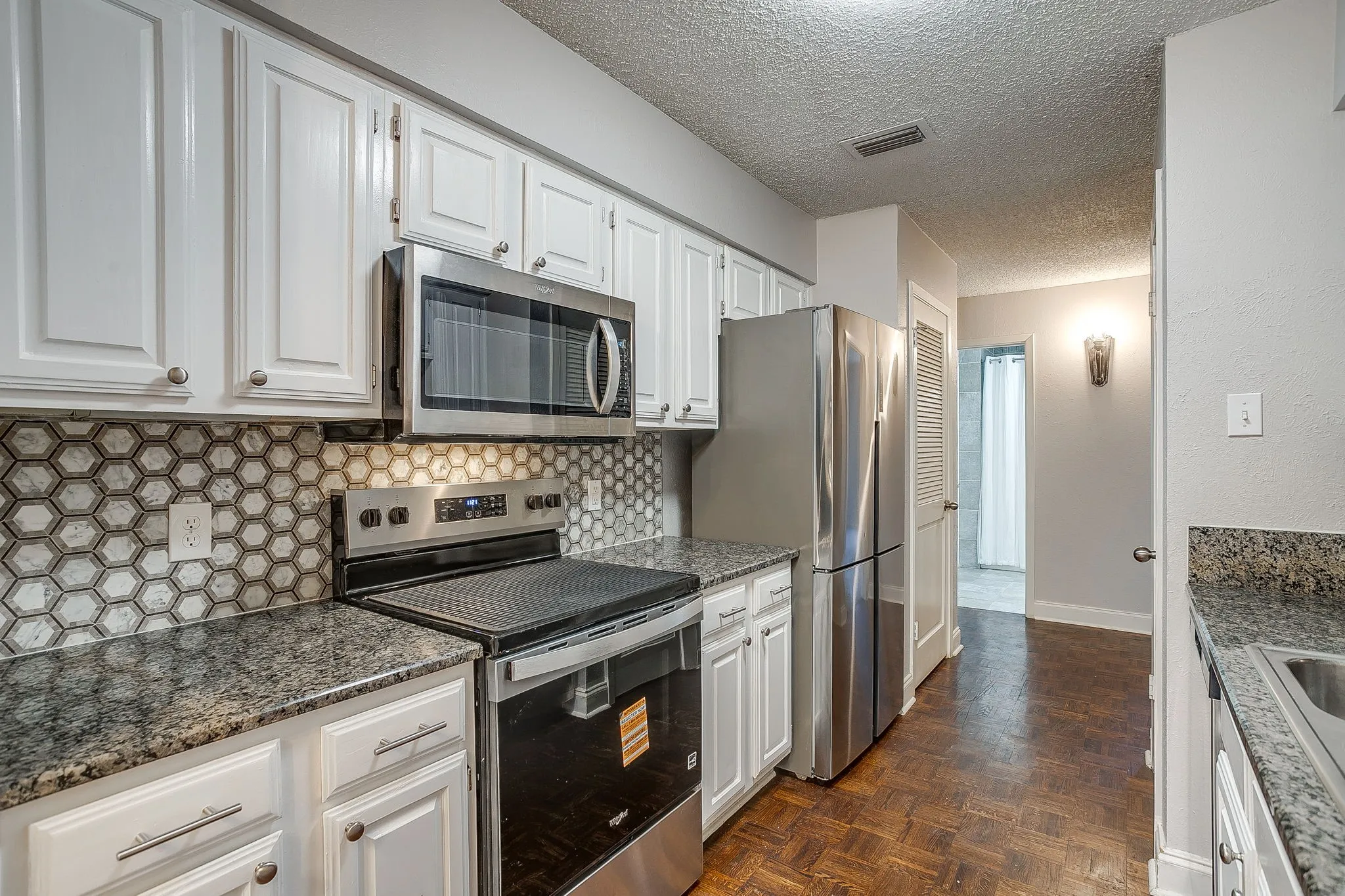 Kitchen featuring white cabinetry, stainless steel appliances, granite-style countertops, and a hexagonal tile backsplash