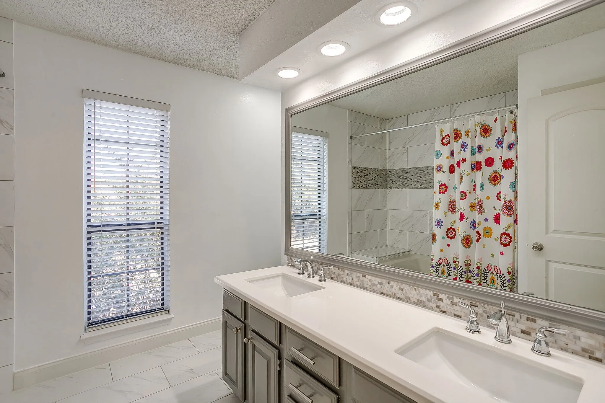 Dual vanity with undermount sinks, chrome faucets, and a speckled tile backsplash