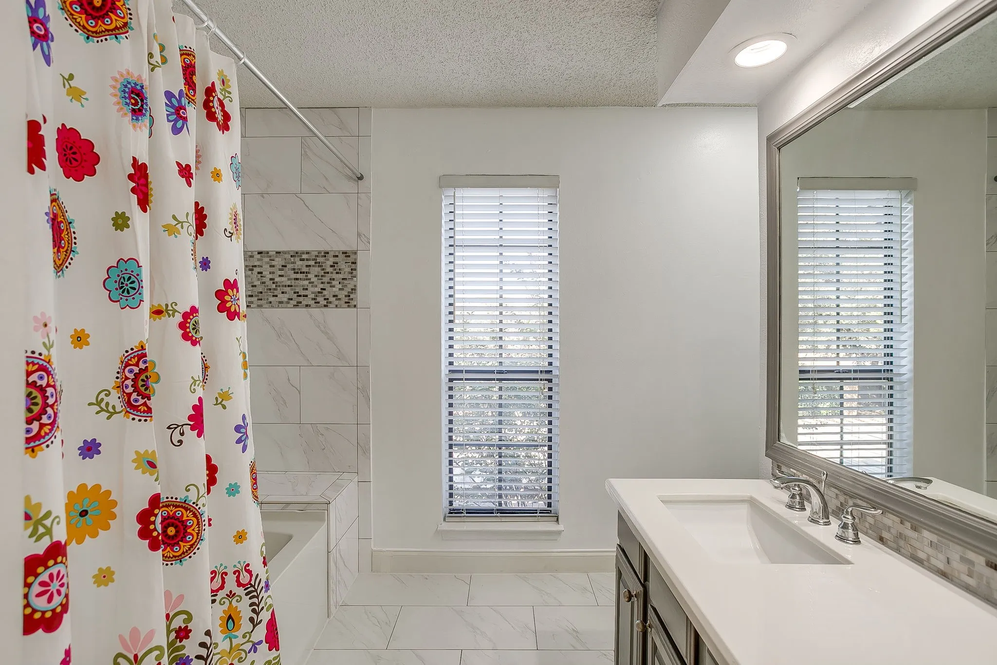 Bathroom featuring a built-in tub with tile surround, mosaic accent tile, a single vanity with an undermount sink, and a framed mirror