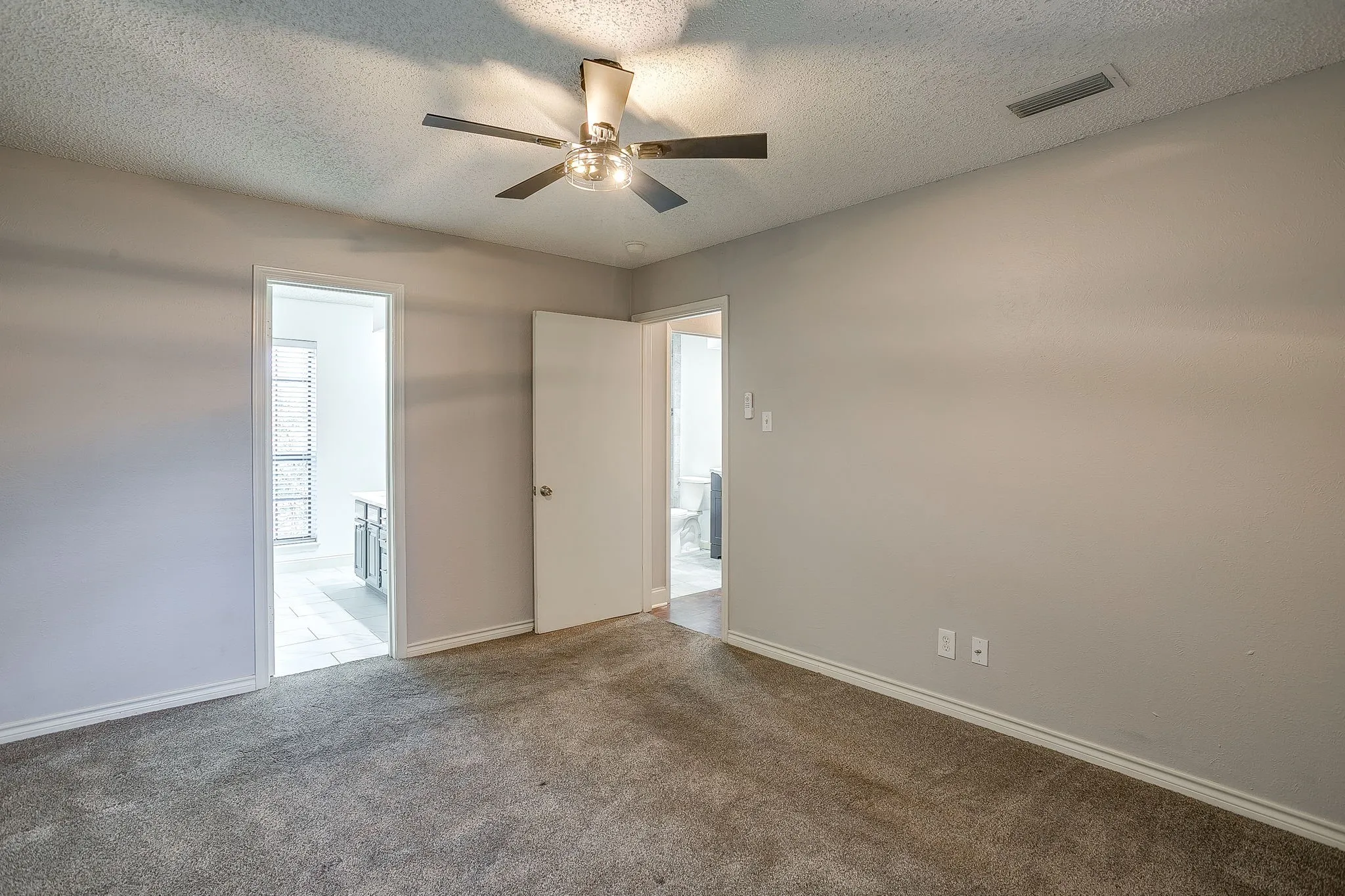 Spacious room featuring neutral carpeting, light-toned wall paint, and a ceiling fan with integrated lighting