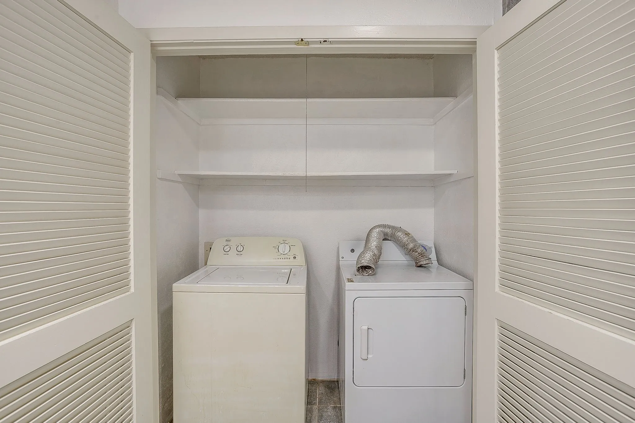 Compact laundry area featuring louvered bi-fold doors, a top-load washing machine, and a front-load dryer