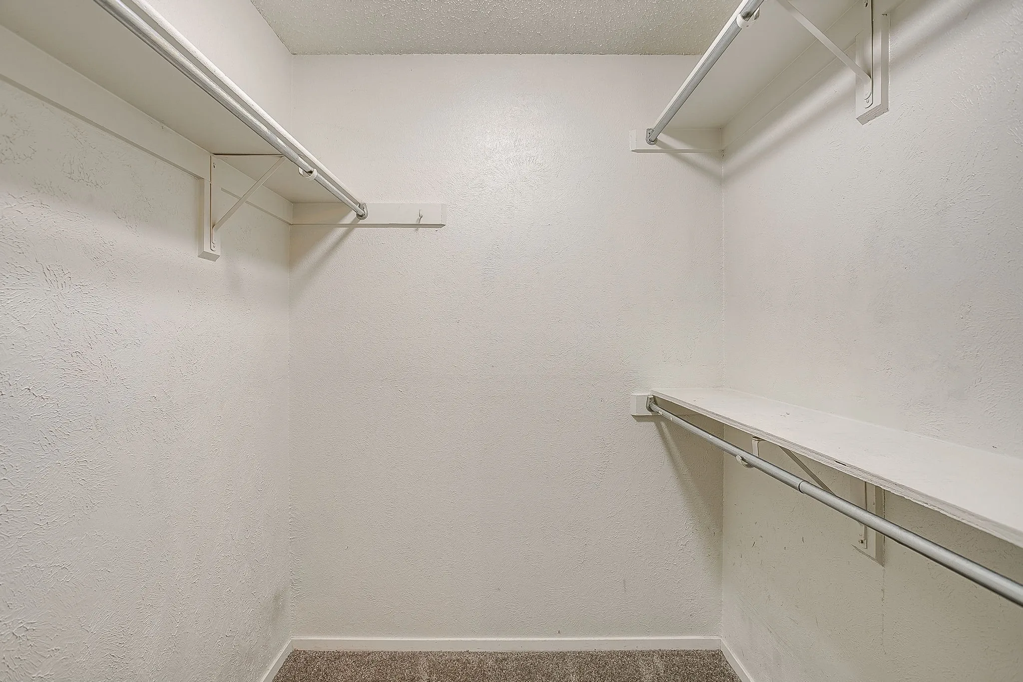 Interior closet featuring white textured walls and carpeting