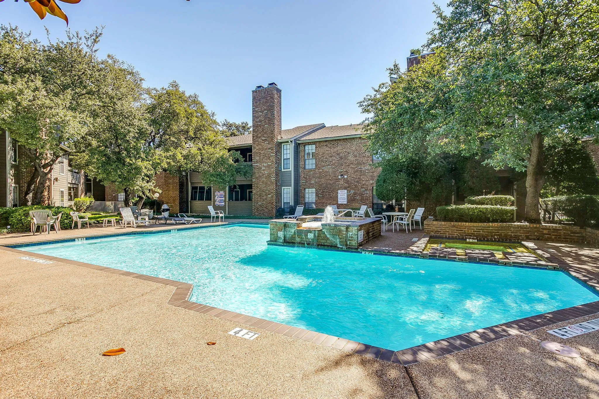 Expansive swimming pool with a stone water feature, surrounded by concrete decking and mature trees
