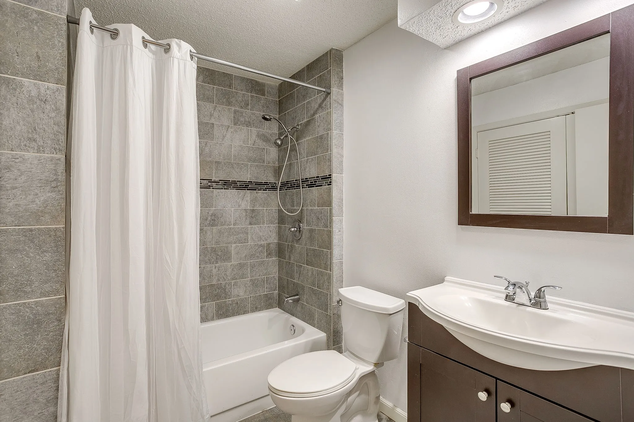 Bathroom featuring a shower-over-tub combination with full-height tile surround and decorative accent band