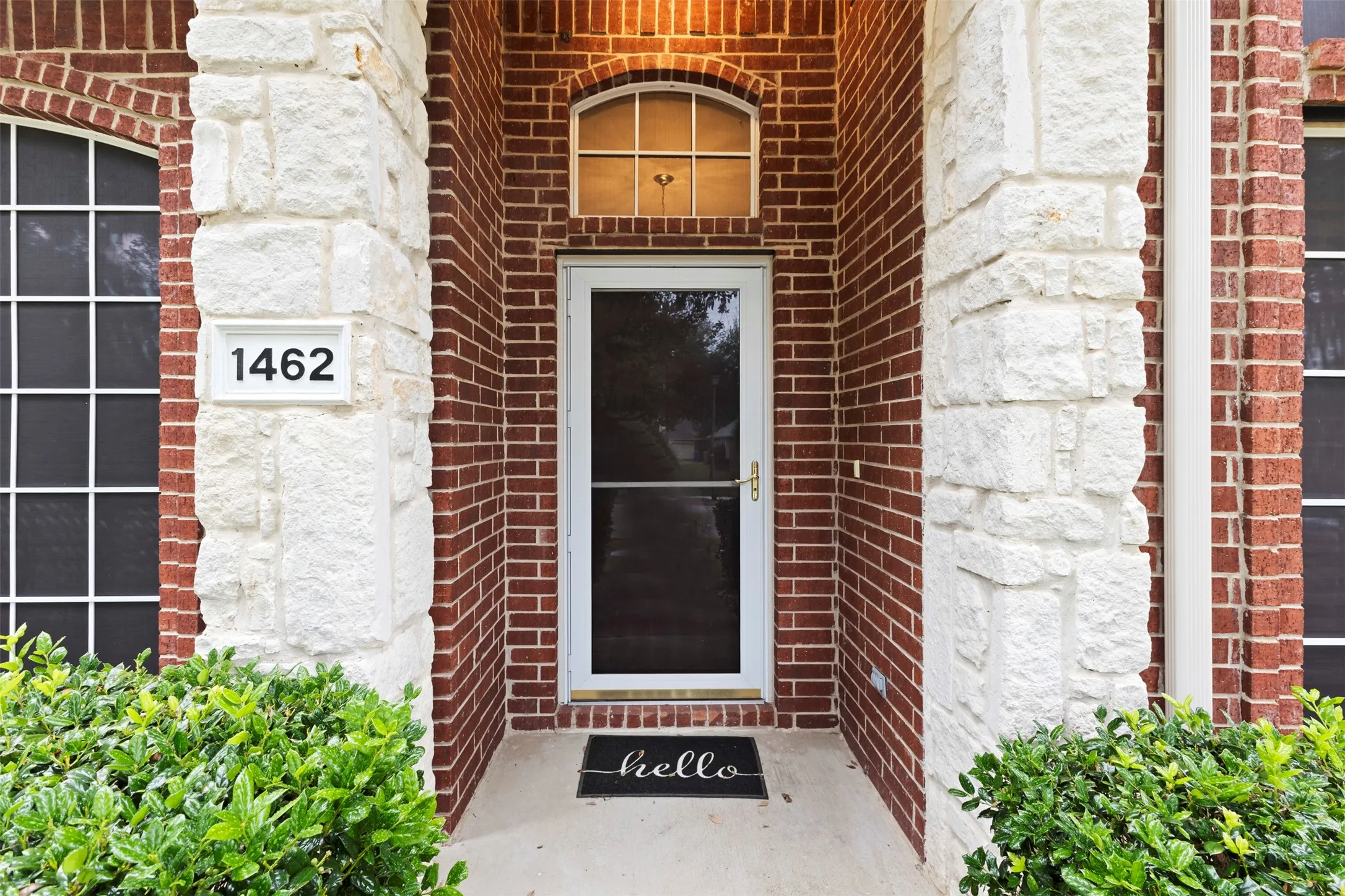 Red brick exterior with stone accents, a white entry door, and an arched transom window