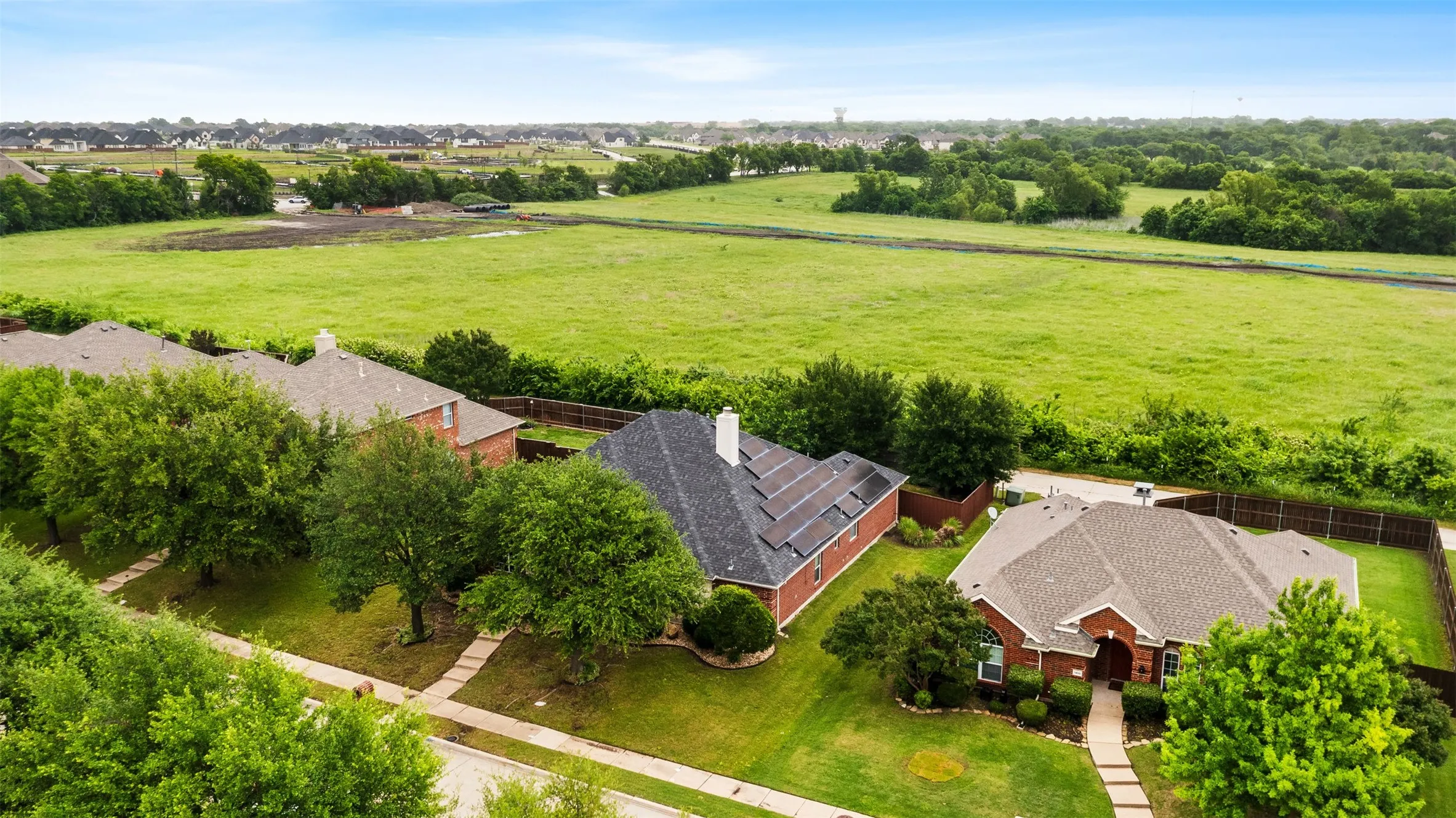 Residential property featuring a red brick exterior, a grey shingled roof, and a mature tree-lined front yard