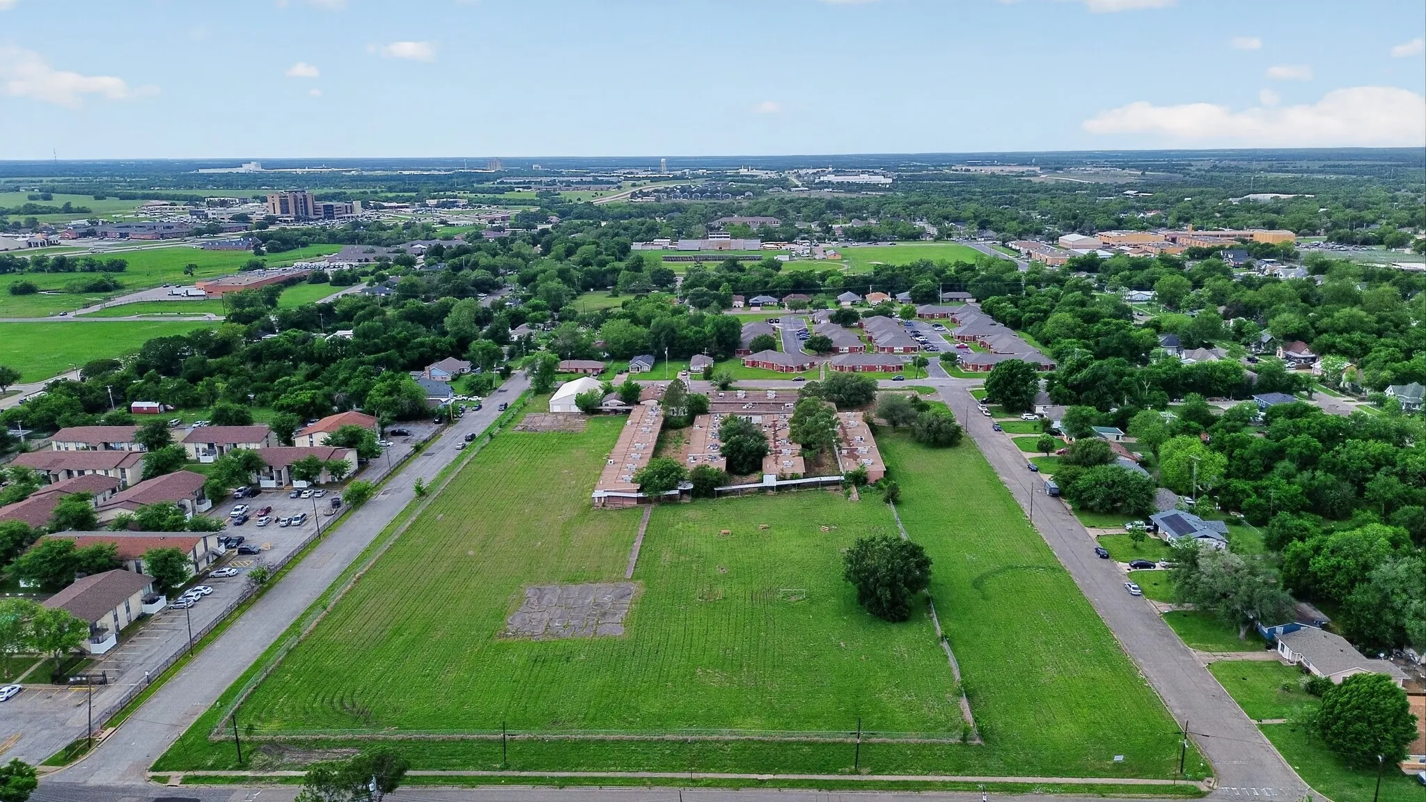 Expansive land parcel featuring open green space, paved road frontage, and established trees