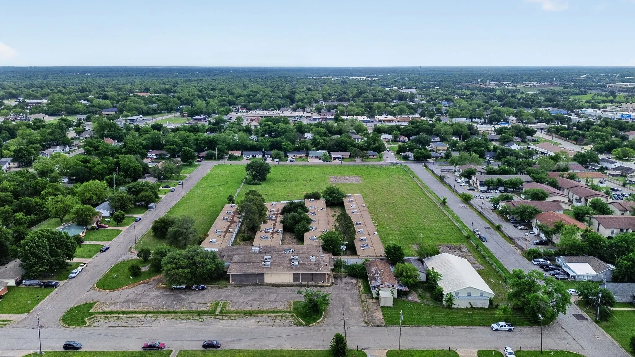 Expansive land parcel featuring multiple structures, surrounded by residential properties and mature trees