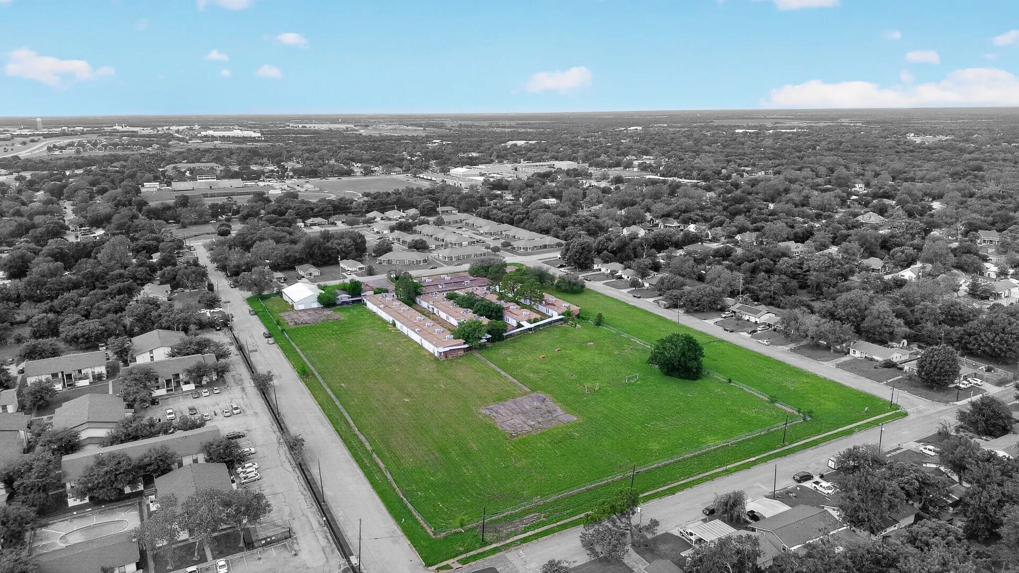 Expansive green space featuring large grass areas, a single mature tree, and perimeter fencing