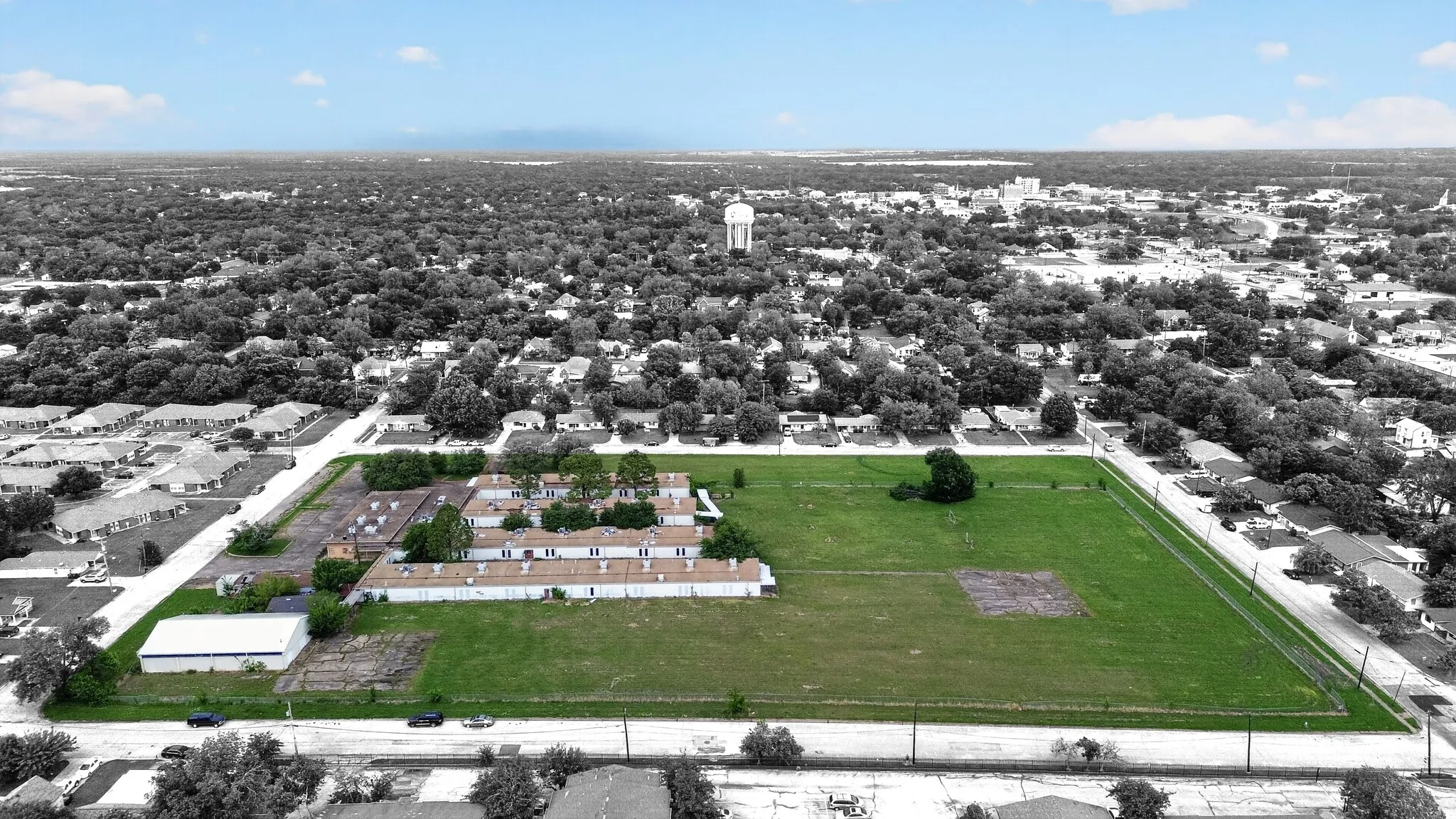 Expansive lot featuring a large green space, existing commercial structures, and surrounding tree-lined residential areas