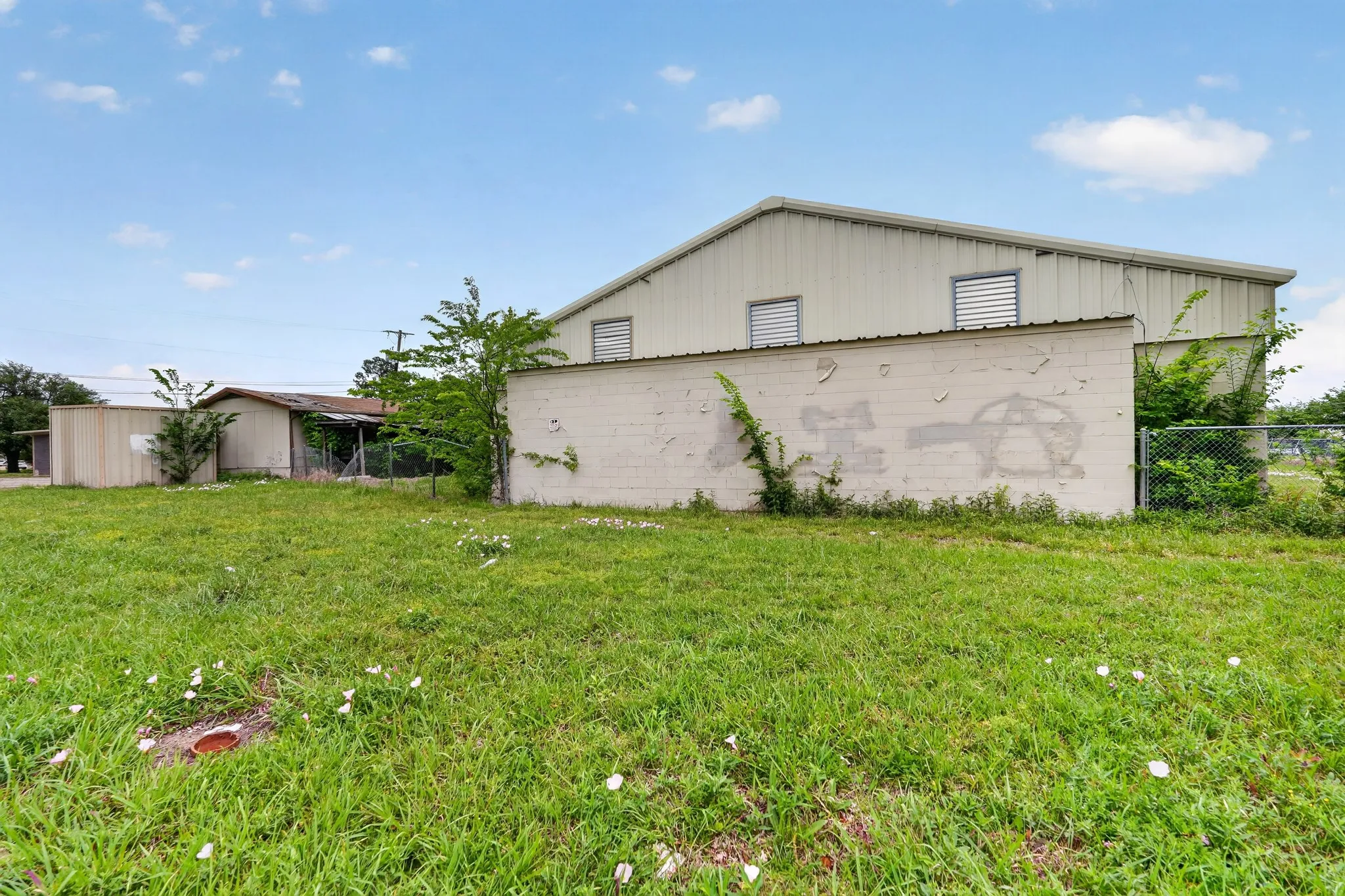 Expansive grass lot bordered by a metal-sided building with a pitched roof and louvered vents
