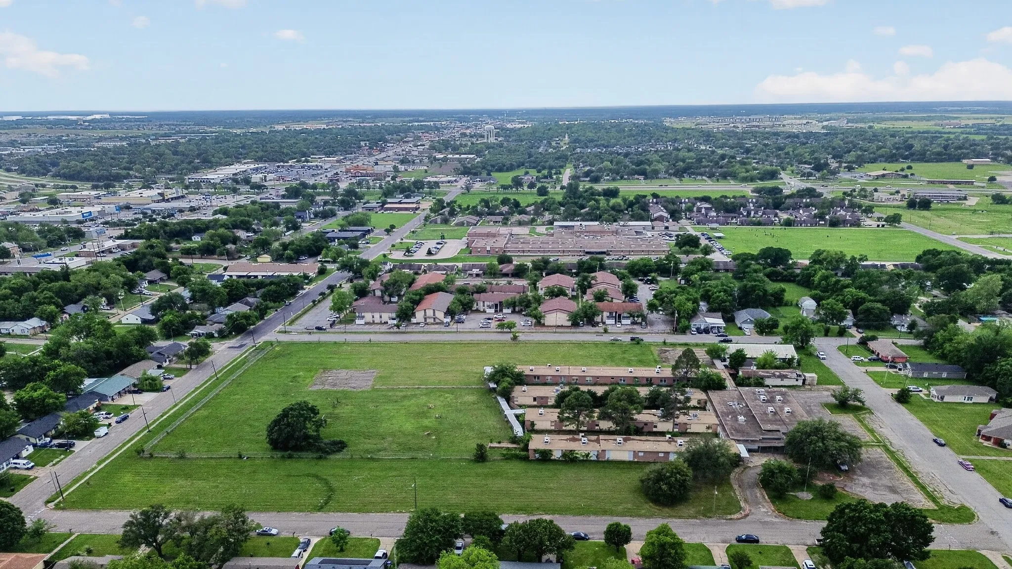 Expansive land parcel featuring open green space, paved road frontage, and scattered mature trees