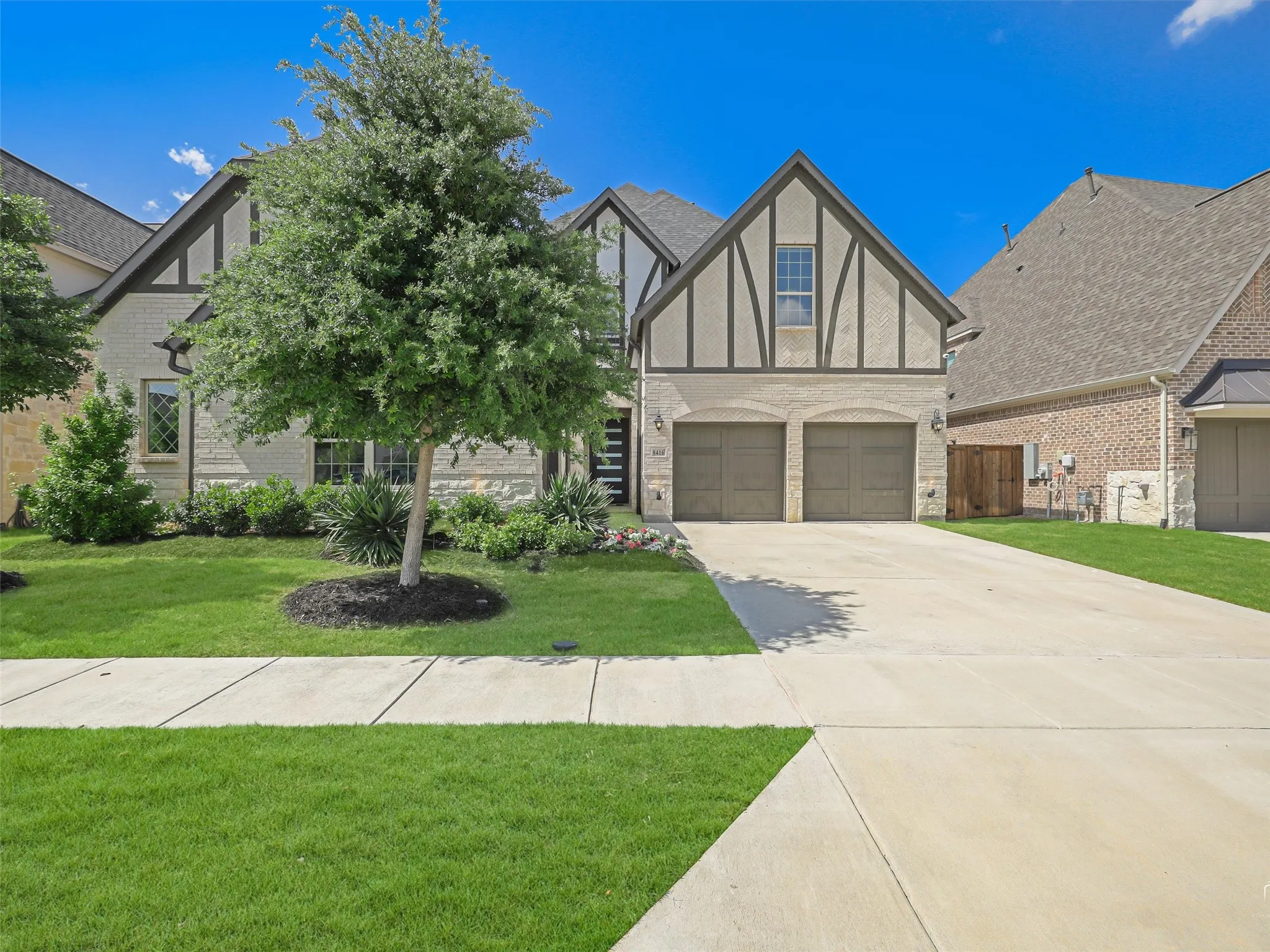 Tudor-style facade featuring light brick and stucco, decorative timber accents, a two-car garage, and a concrete driveway