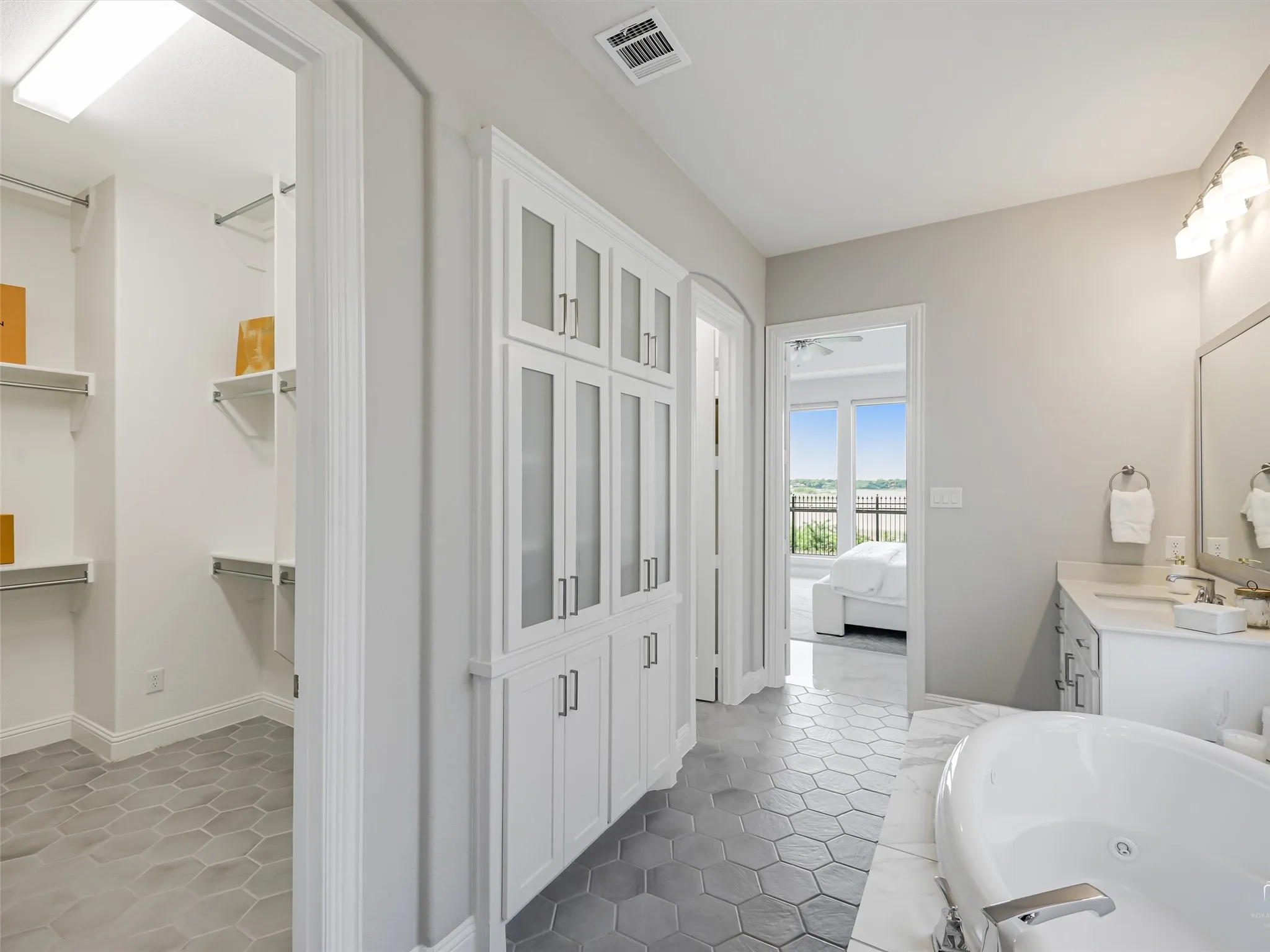 Contemporary bathroom featuring hexagonal tile flooring, freestanding soaking tub, and a built-in linen cabinet with frosted glass doors