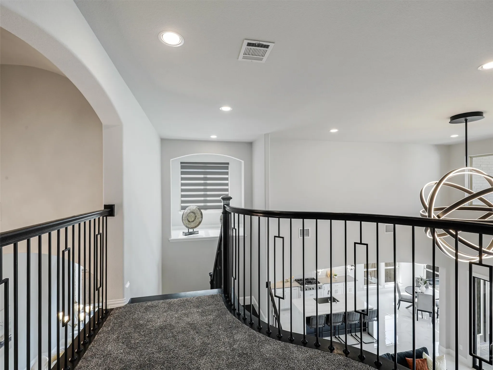 Second-level landing featuring contemporary black wrought iron railings, recessed lighting, arched doorways, a unique spherical chandelier, and a curved staircase with carpeted treads