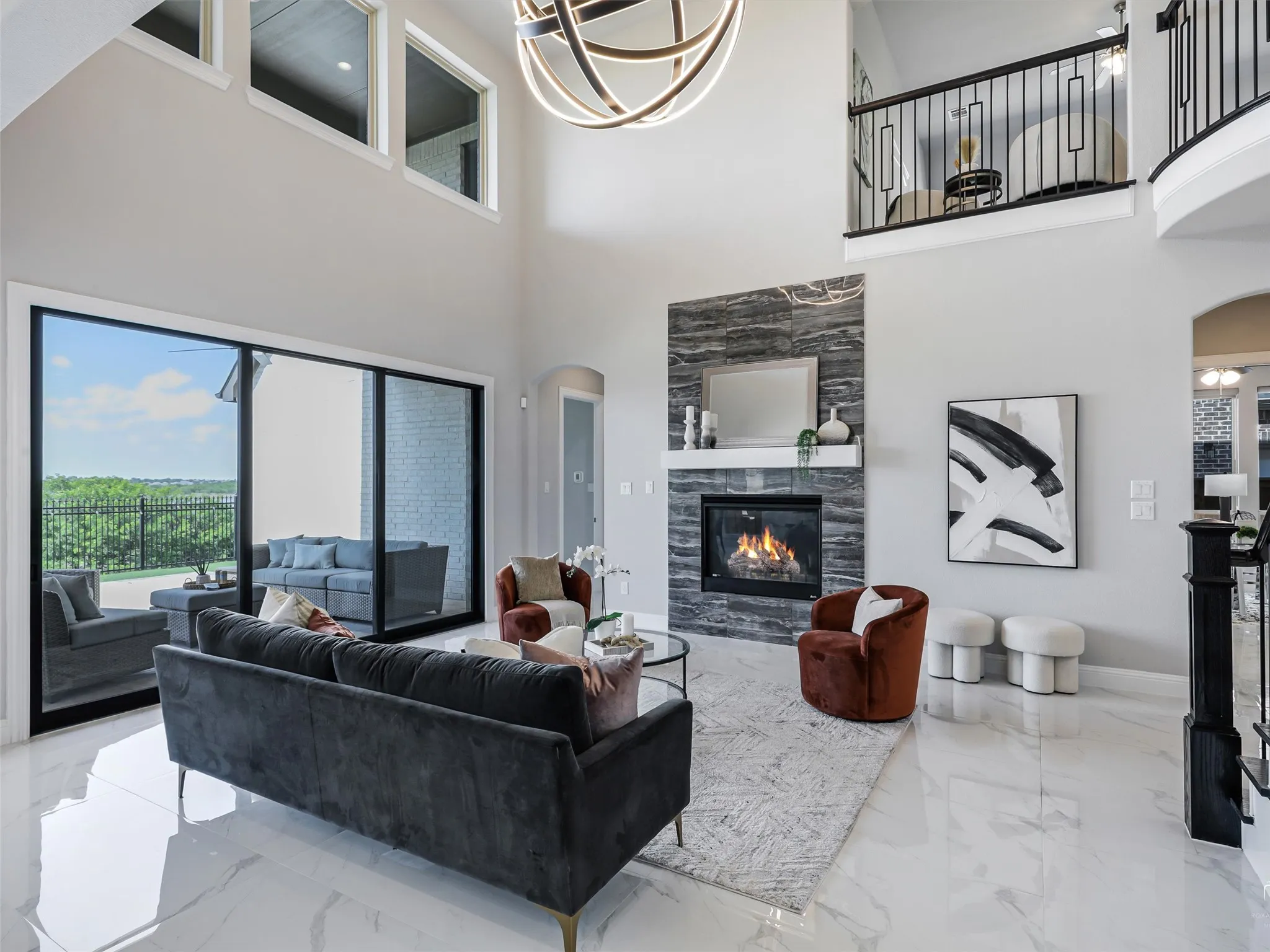 Spacious living area featuring high ceilings, large sliding glass doors, a stone-clad fireplace with a mantle, a second-story balcony with metal railings, and polished tile flooring
