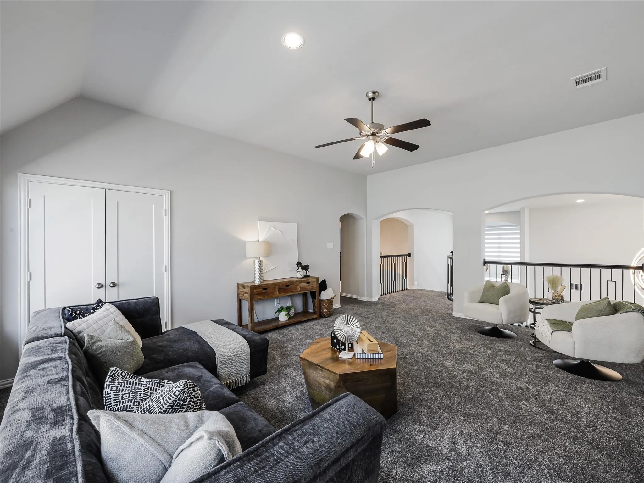 Spacious second-story room featuring vaulted ceilings, a ceiling fan with integrated lighting, and plush grey carpet