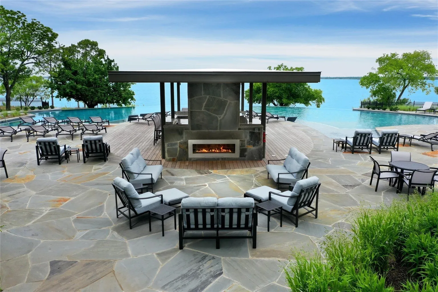 Expansive outdoor patio featuring irregular flagstone paving, a covered structure with a built-in linear fireplace, and a wood-finish deck