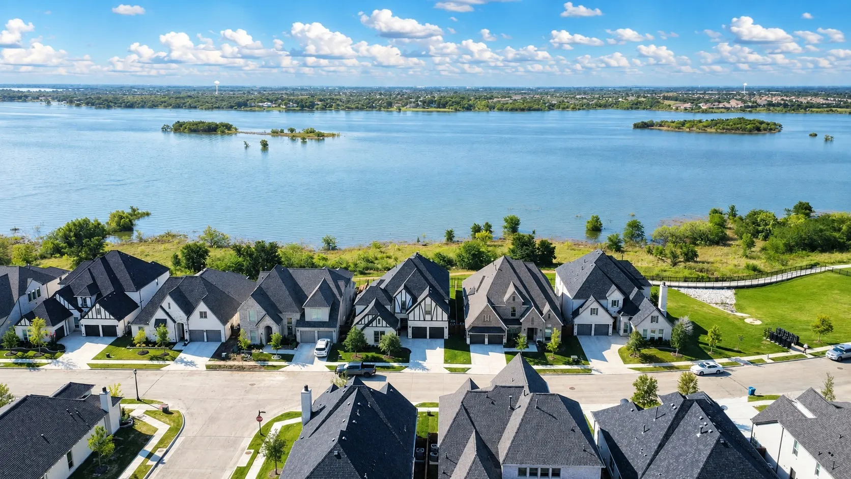 Residential properties featuring diverse architectural styles, situated along a large body of water, with landscaped green spaces and an established street grid