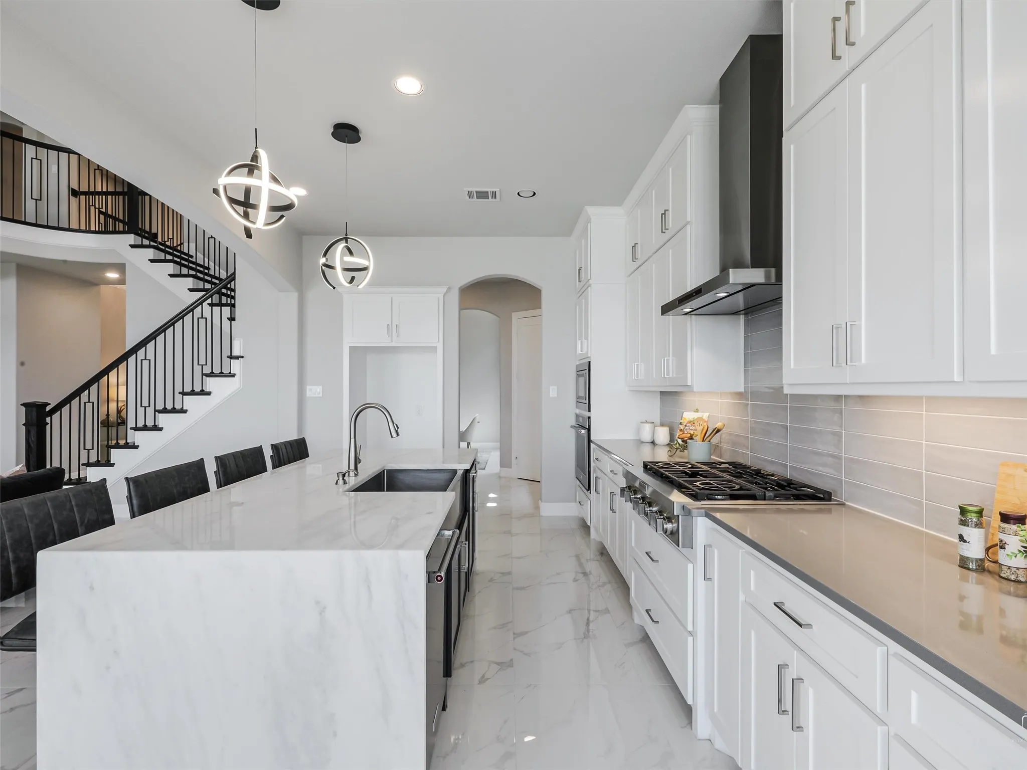 Modern kitchen featuring a large island with white veined countertop, stainless steel sink, and contemporary pendant lighting