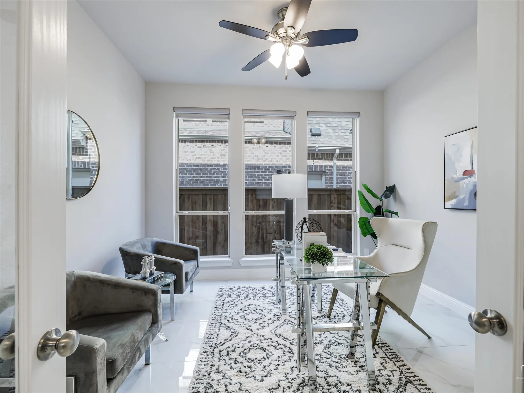Bright room featuring three tall windows, a ceiling fan with light fixture, white tile flooring, and light gray walls