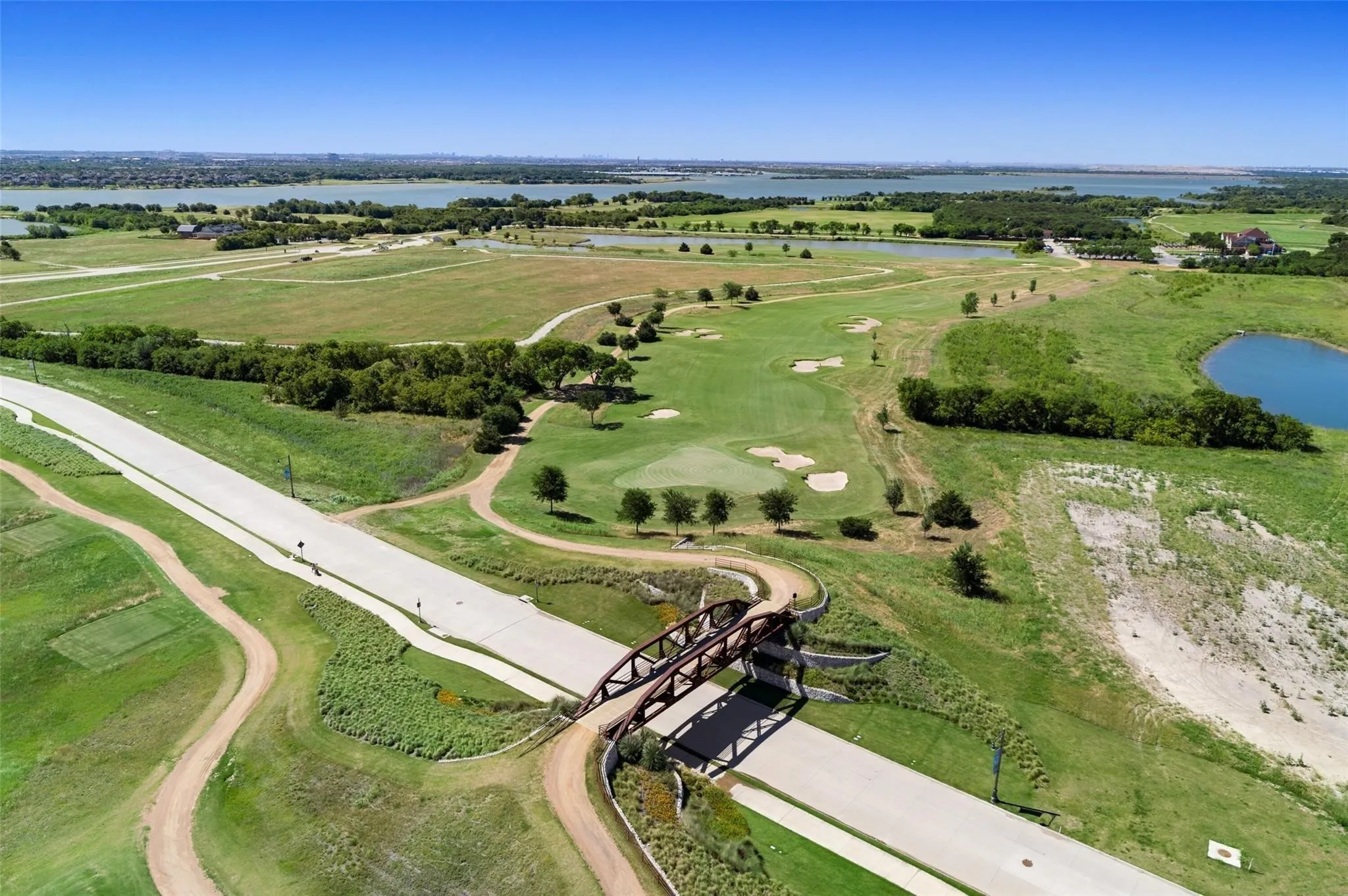 Expansive aerial showcasing a golf course with multiple greens and sand traps, surrounded by mature trees and natural landscaping