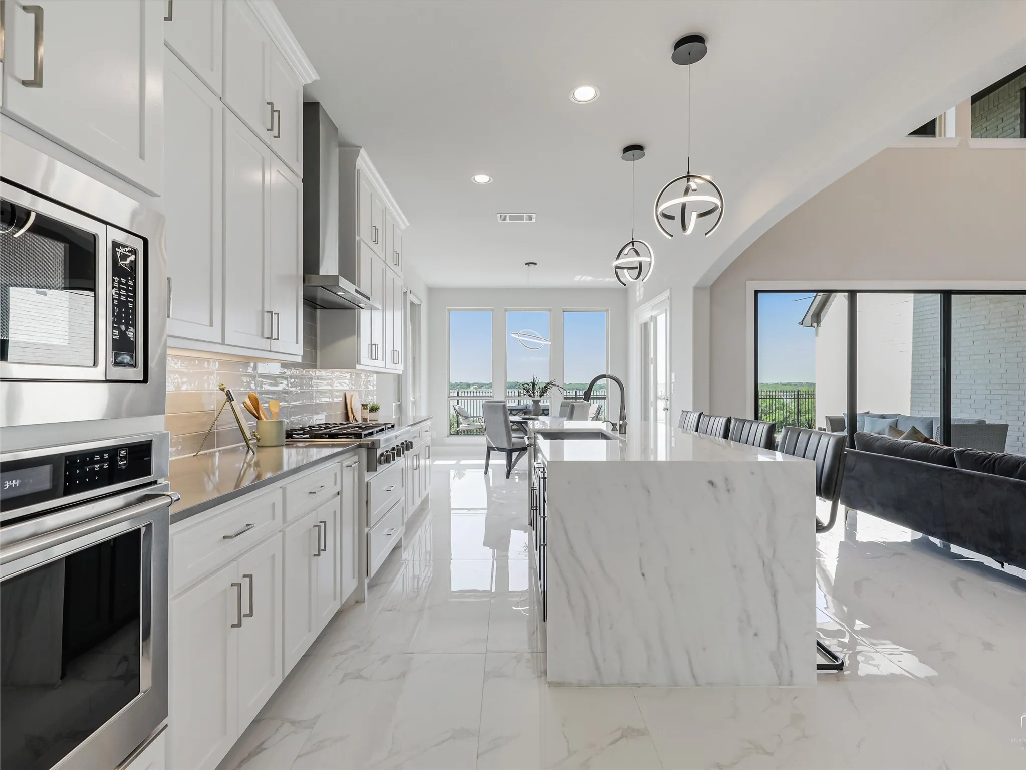 Open-concept kitchen featuring white shaker cabinetry, stainless steel appliances, and a waterfall-edge island with seating