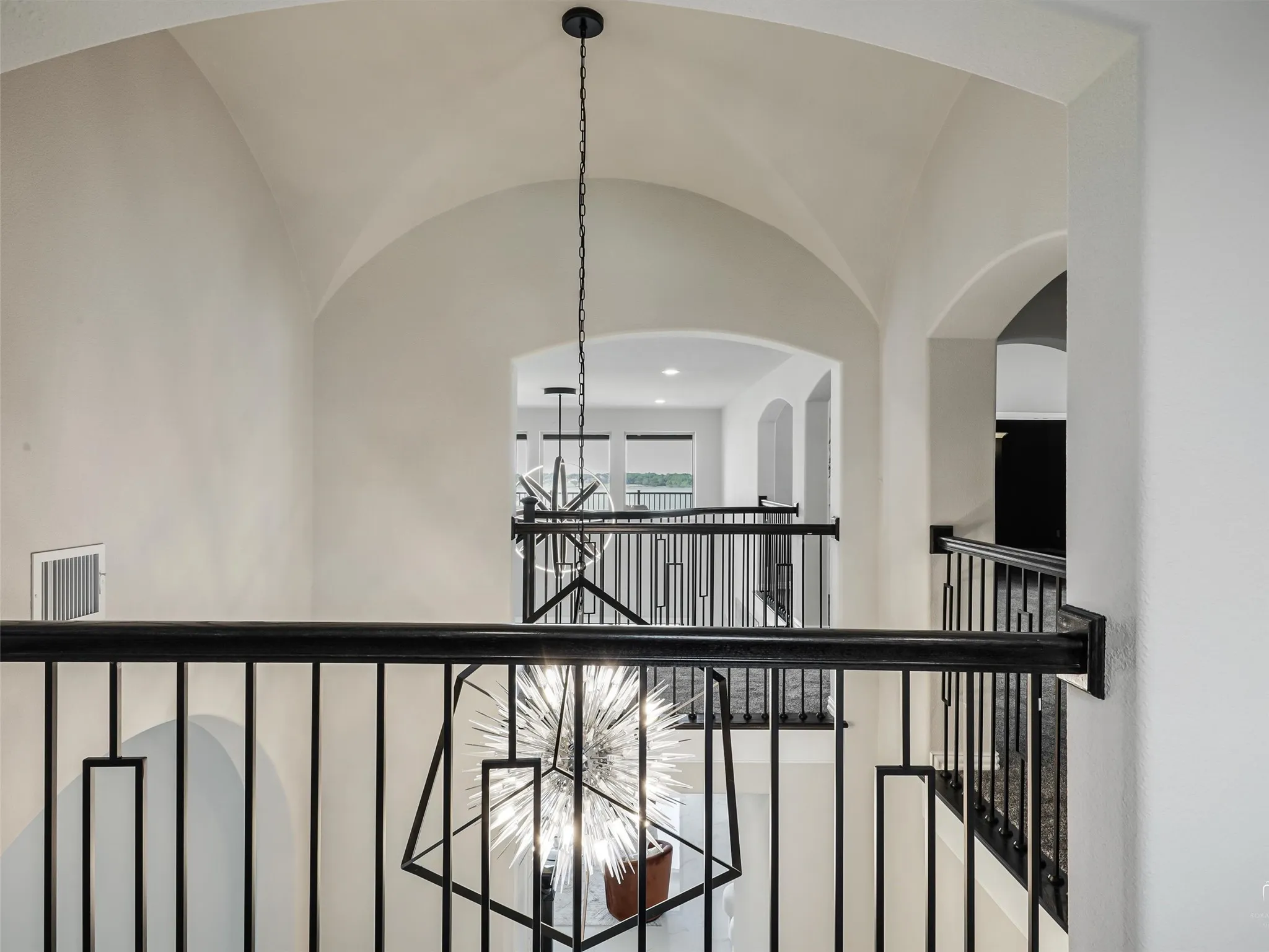 Architectural archways and vaulted ceilings define this upper-level hallway, featuring wrought iron railings with geometric accents