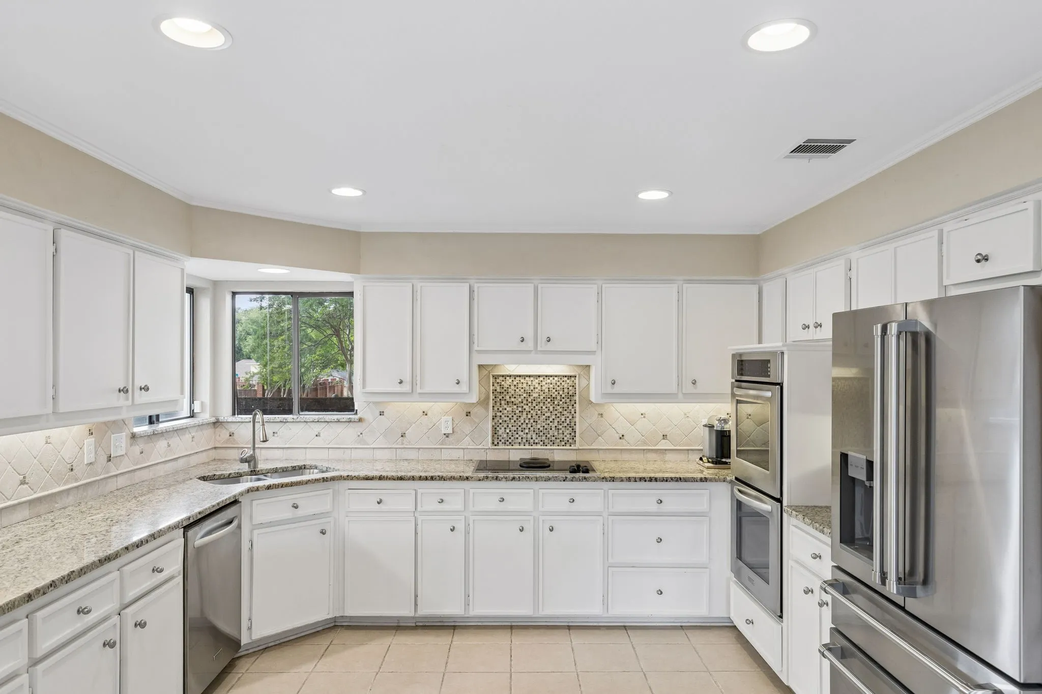 Kitchen featuring white cabinetry, light-toned countertops, tile flooring, and stainless steel appliances including a refrigerator, double oven, and dishwasher